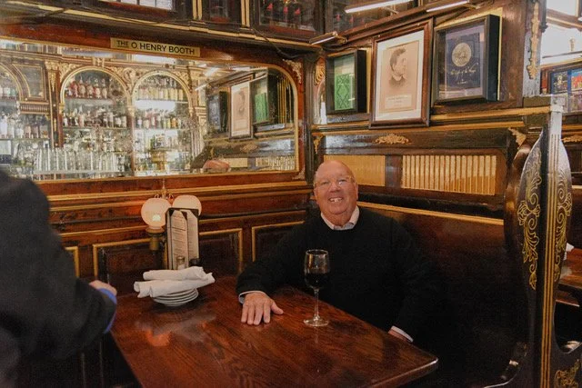 Author E. J. Simon sitting in a booth at Pete's Tavern with a glass of wine