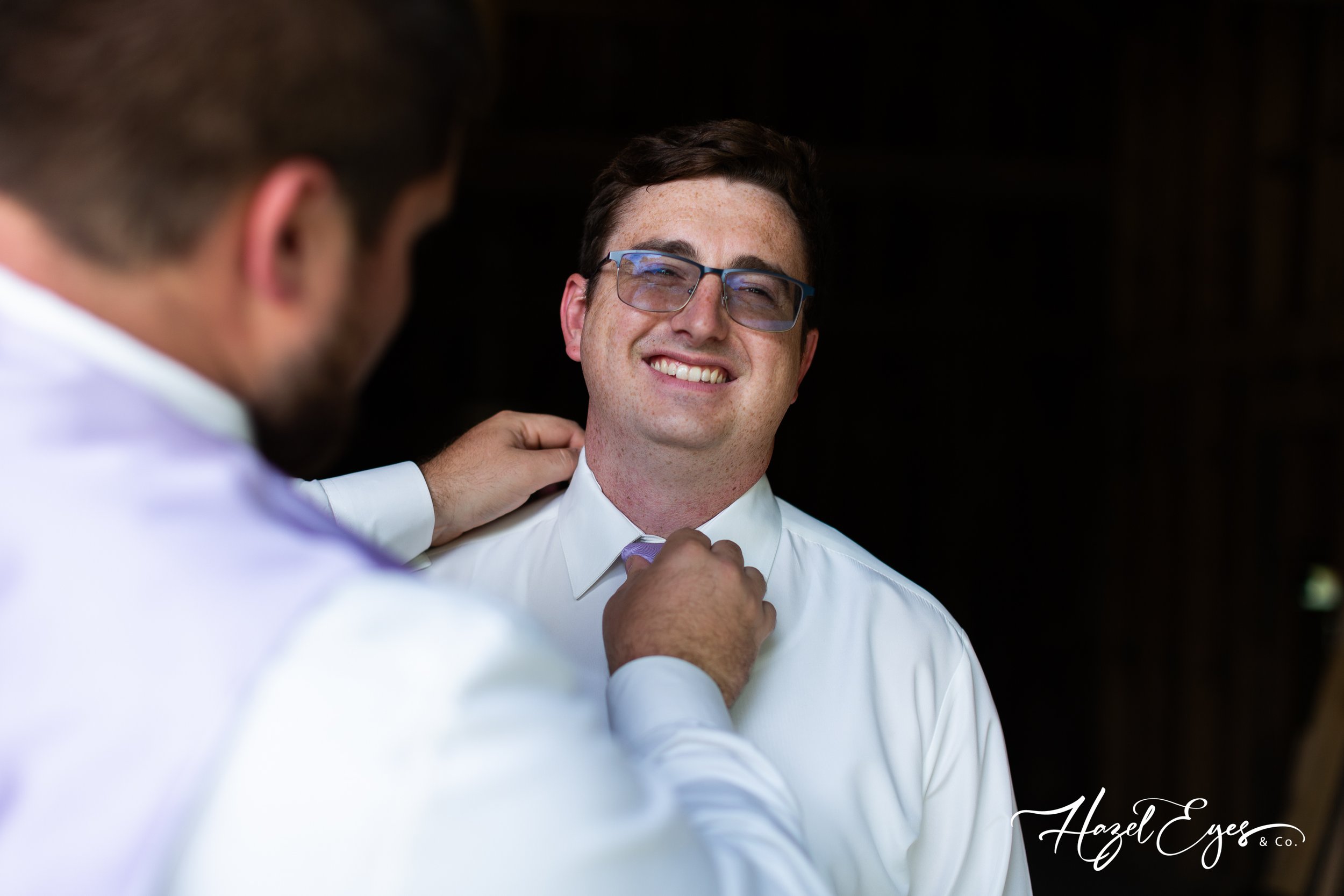 Best man helping groom with tie.