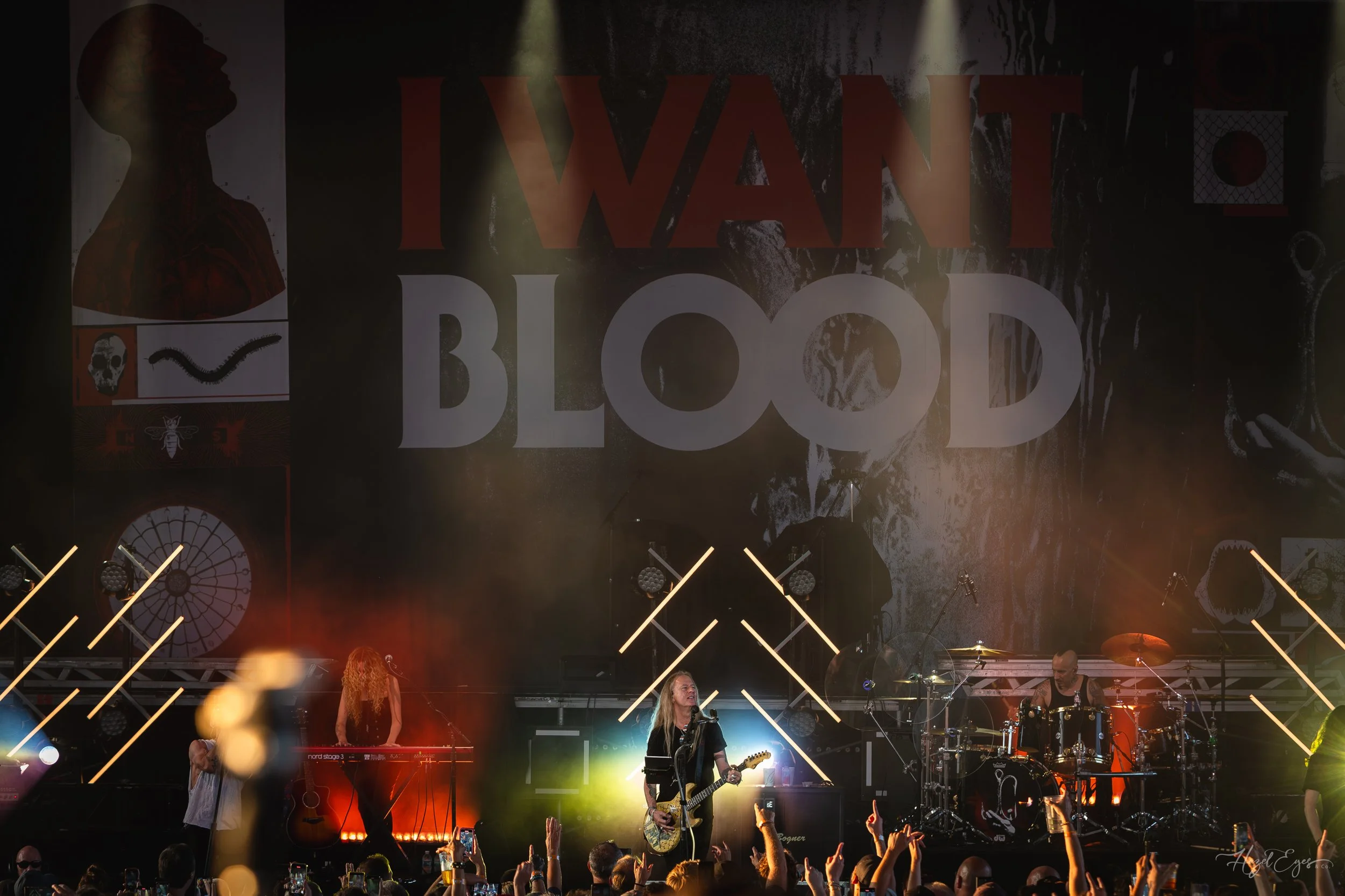 Jerry Cantrell in concert at Michigan Lottery Amphitheatre at Freedom Hill in Sterling Heights, MI on August 16, 2024. Guitarist on stage backlit with bright stage lighting with audience in foreground. Full stage shot with the "I WANT BLOOD" stage ba