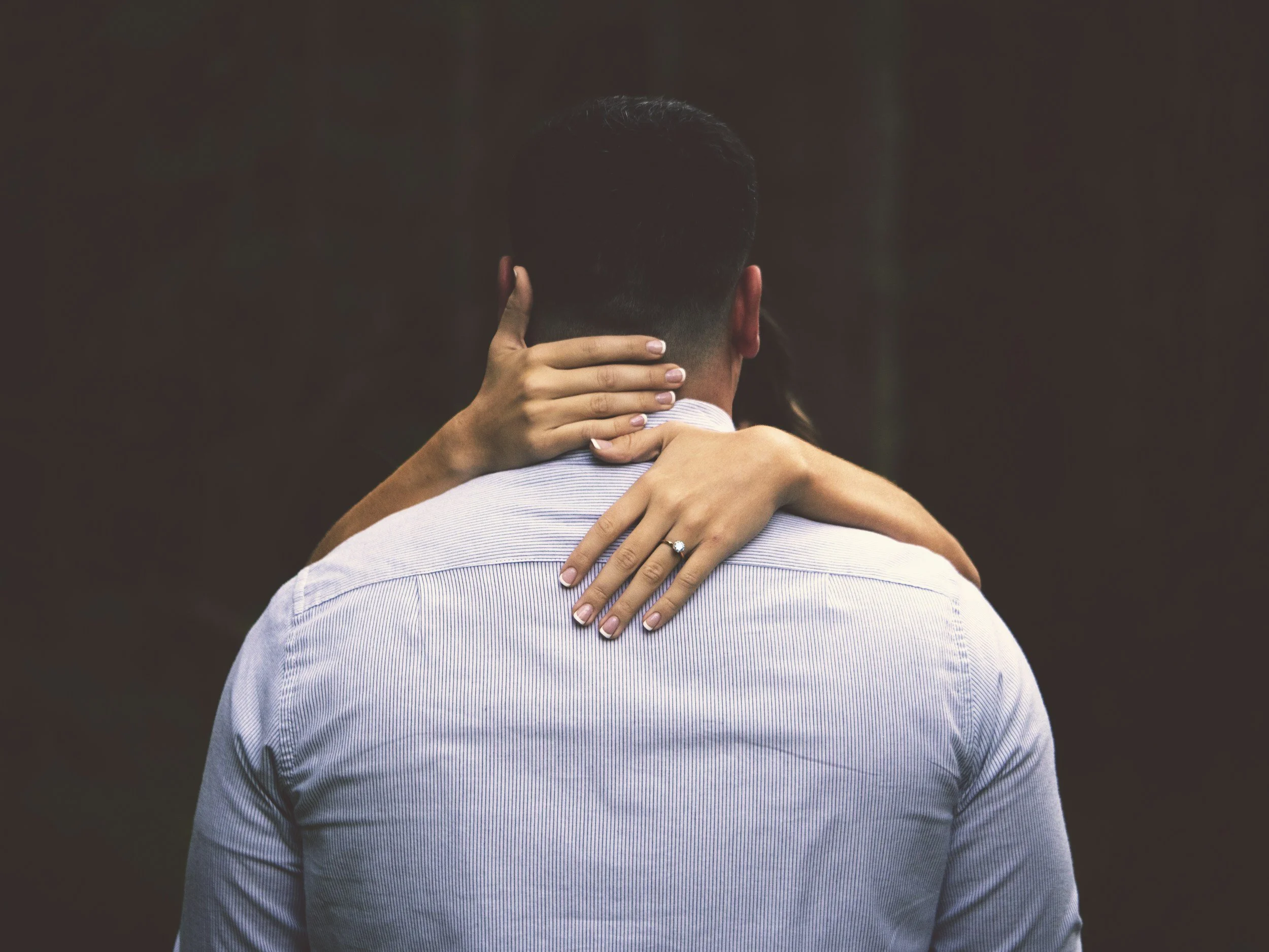 A man and woman hugging, with the woman’s hand showing an engagement ring.