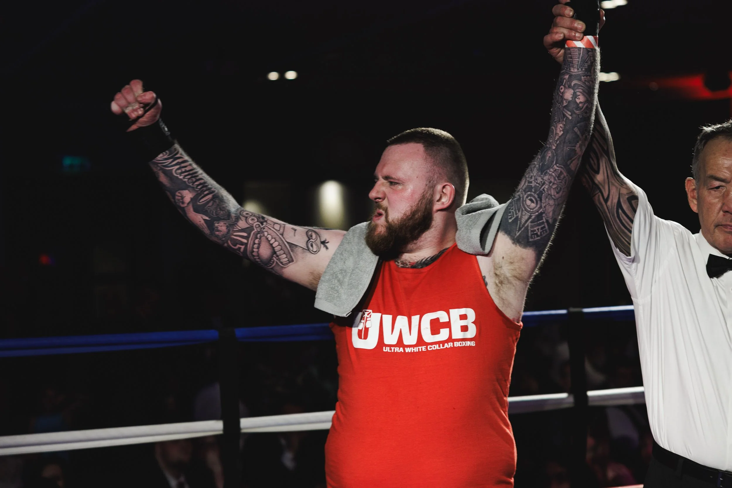 A boxer with tattoos raising his arms in victory while a referee holds his hand in a boxing ring.
