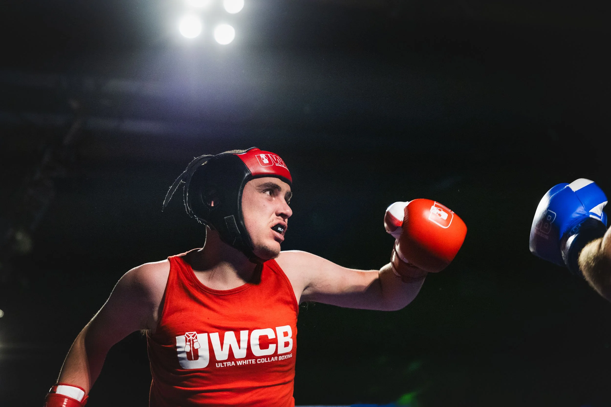 A male boxer wearing red gloves, red sleeveless shirt with 'WCB' logo, and a red headgear, throwing a punch in a boxing match.