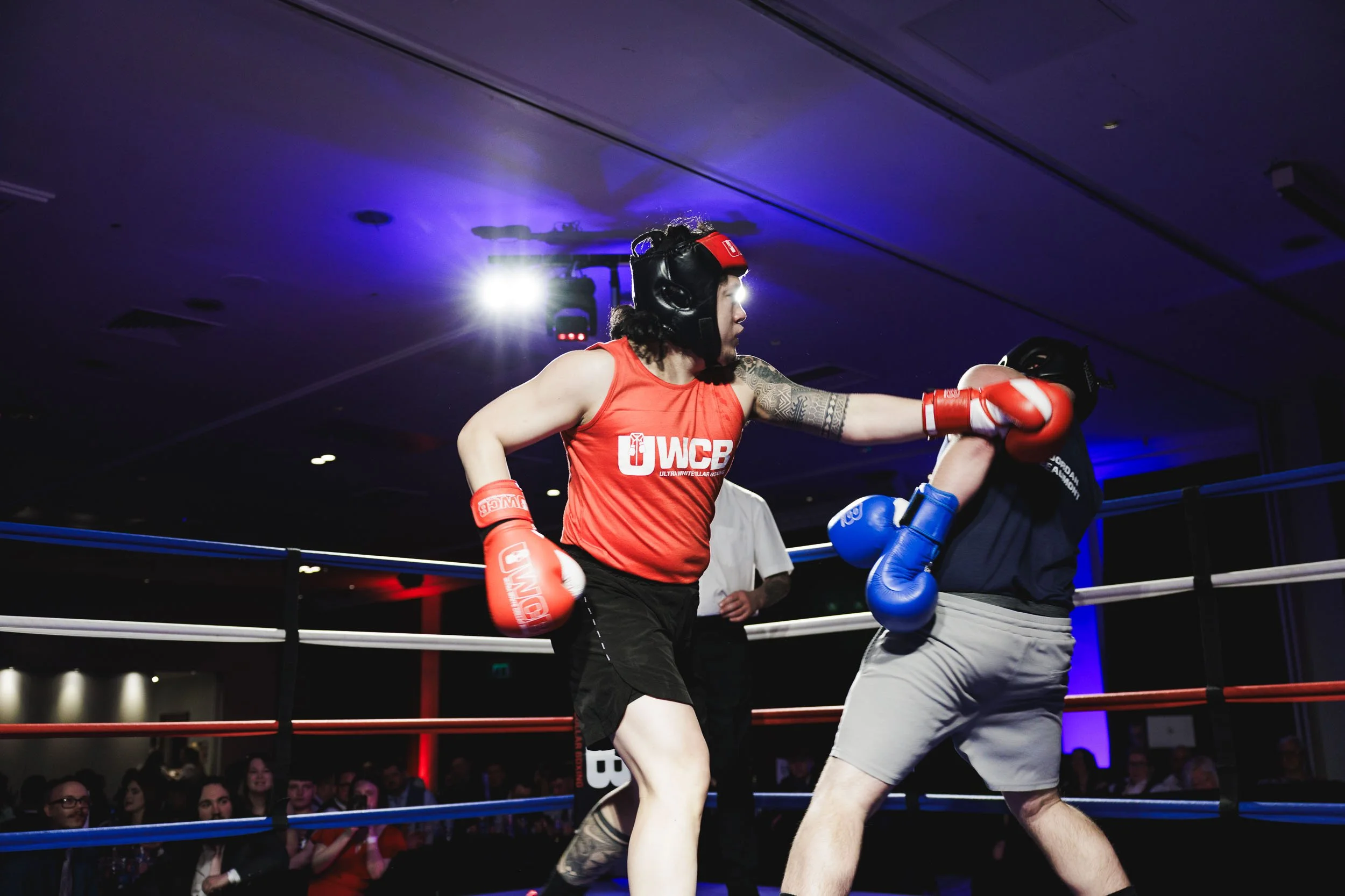 Female boxer throwing a punch at her opponent in a boxing ring during a match, with onlookers watching in the background.