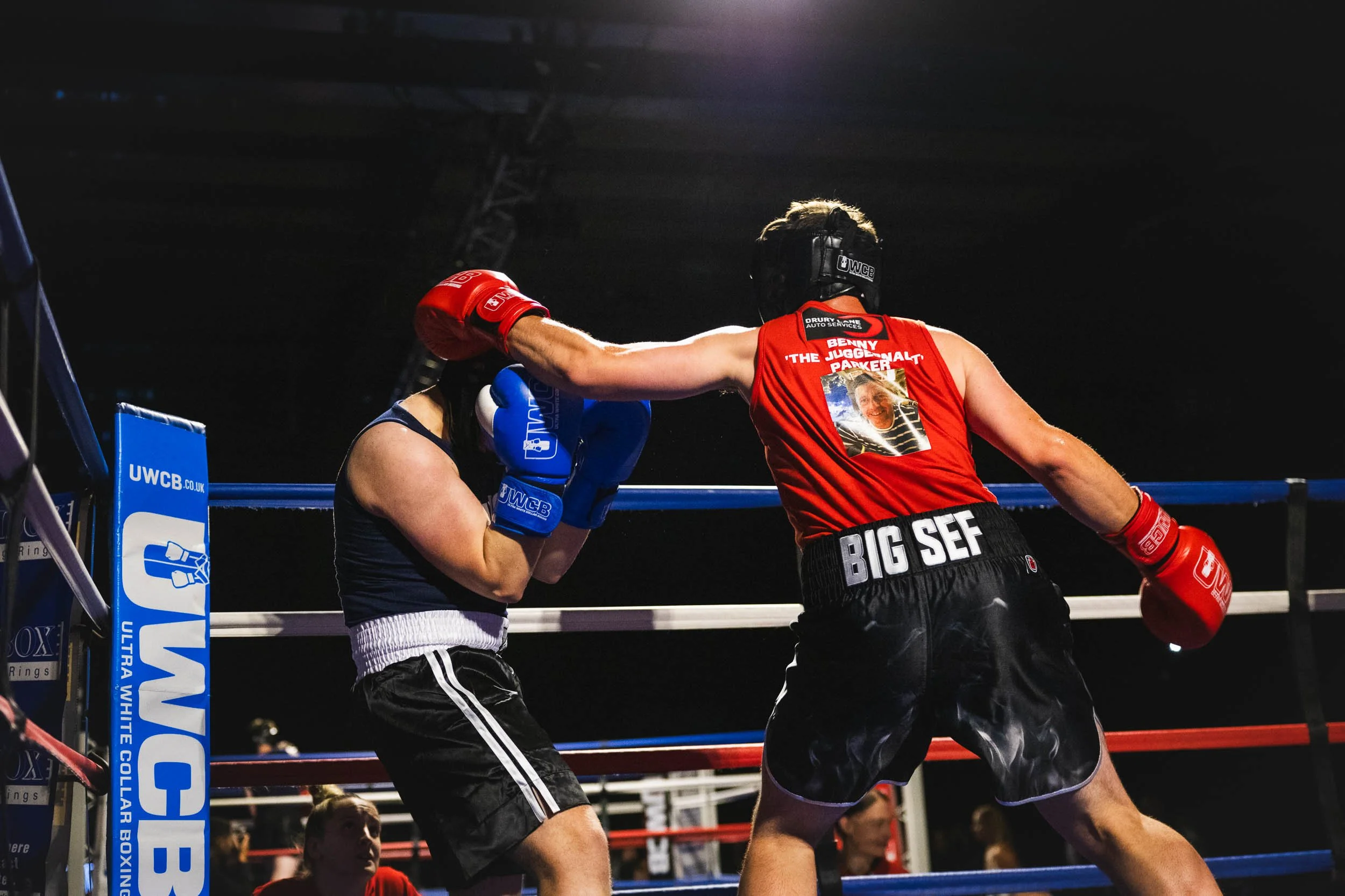 Two women boxers in a ring, one wearing red gloves and a red tank top, the other wearing blue gloves and black shorts, engaged in a boxing match.