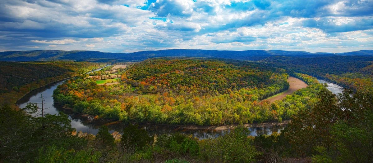 A river winding through a landscape of trees, hills, and farmland under a partly cloudy sky.