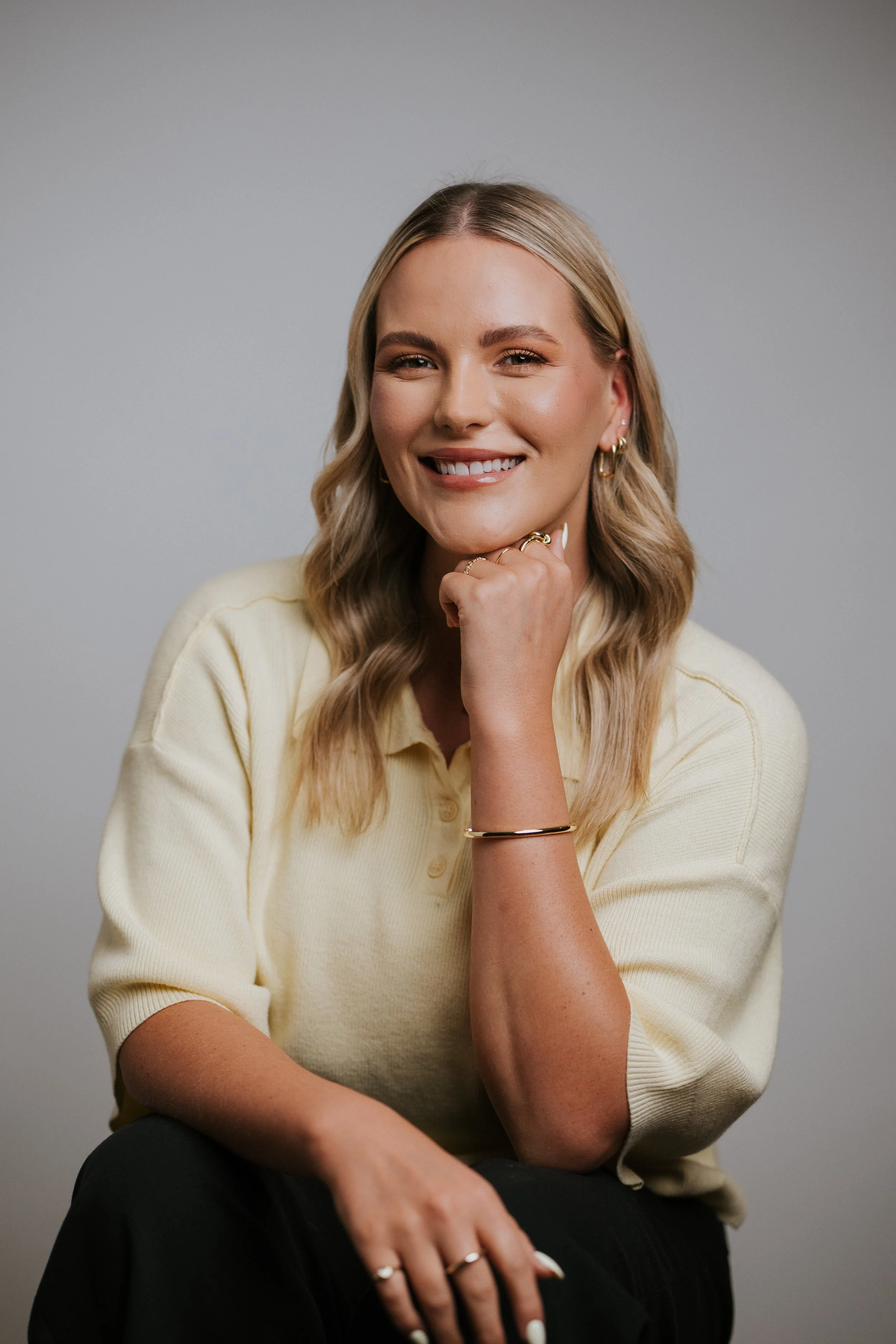 Newport Beach therapist. Orange County therapist. A young woman with blonde, wavy hair wearing a white blouse, smiling, with a neutral gray background.