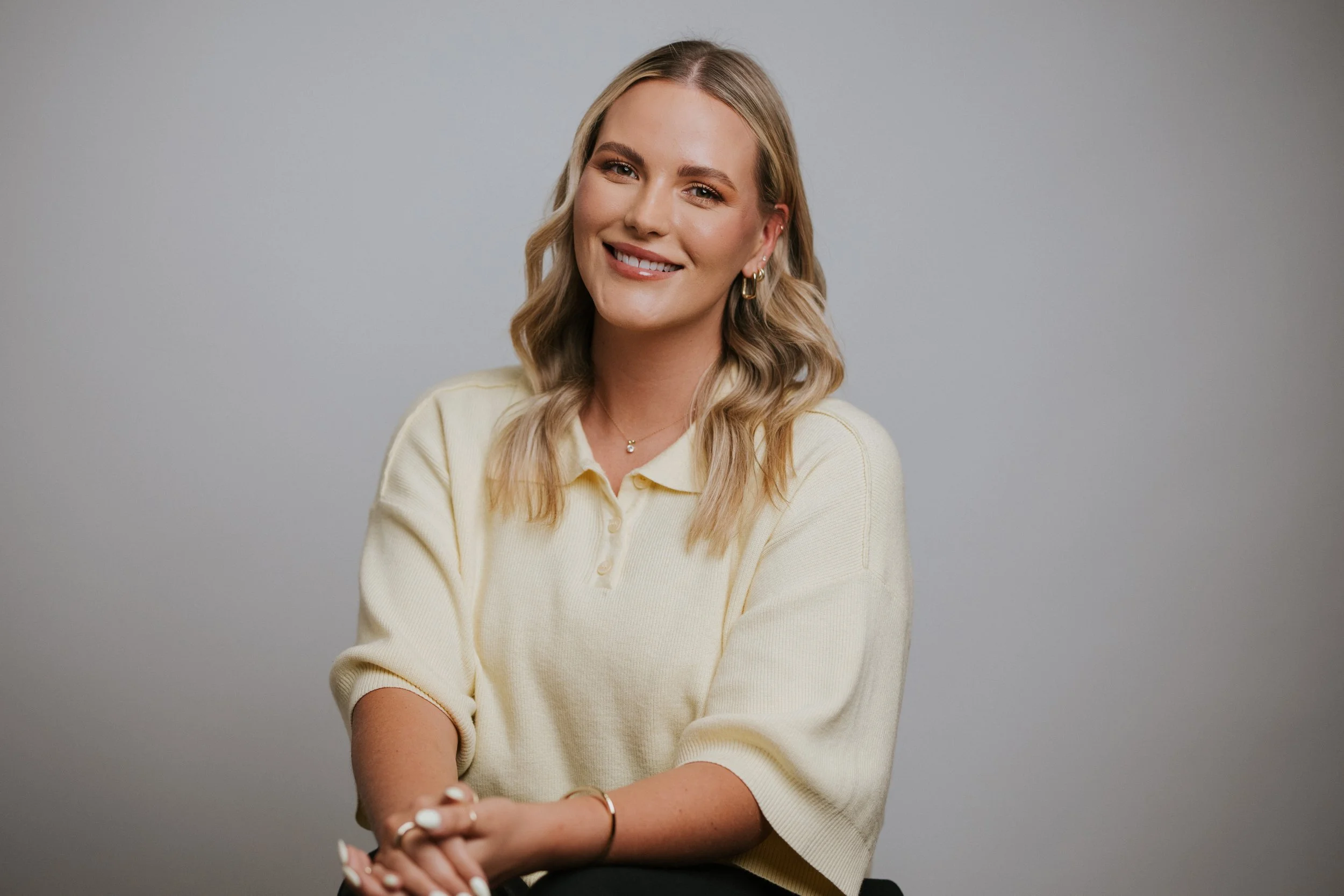 Newport Beach therapist. Orange County therapist. A young woman with blonde wavy hair smiling and wearing a white top against a plain gray background.