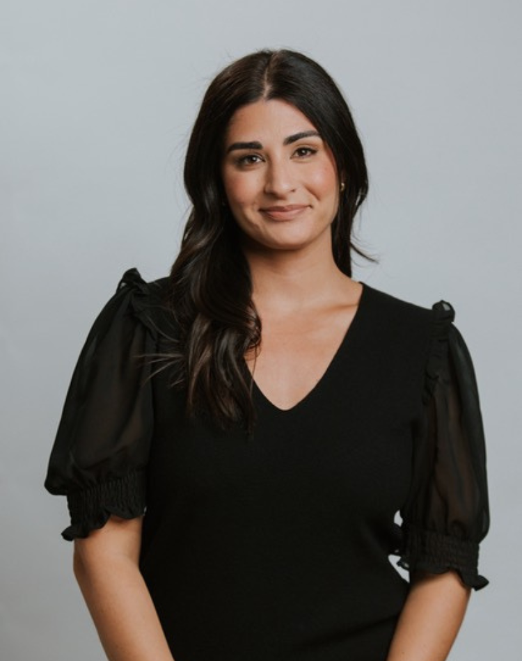 A young woman with long dark hair, wearing a black top with puffy sleeves, smiling softly at the camera against a plain gray background.