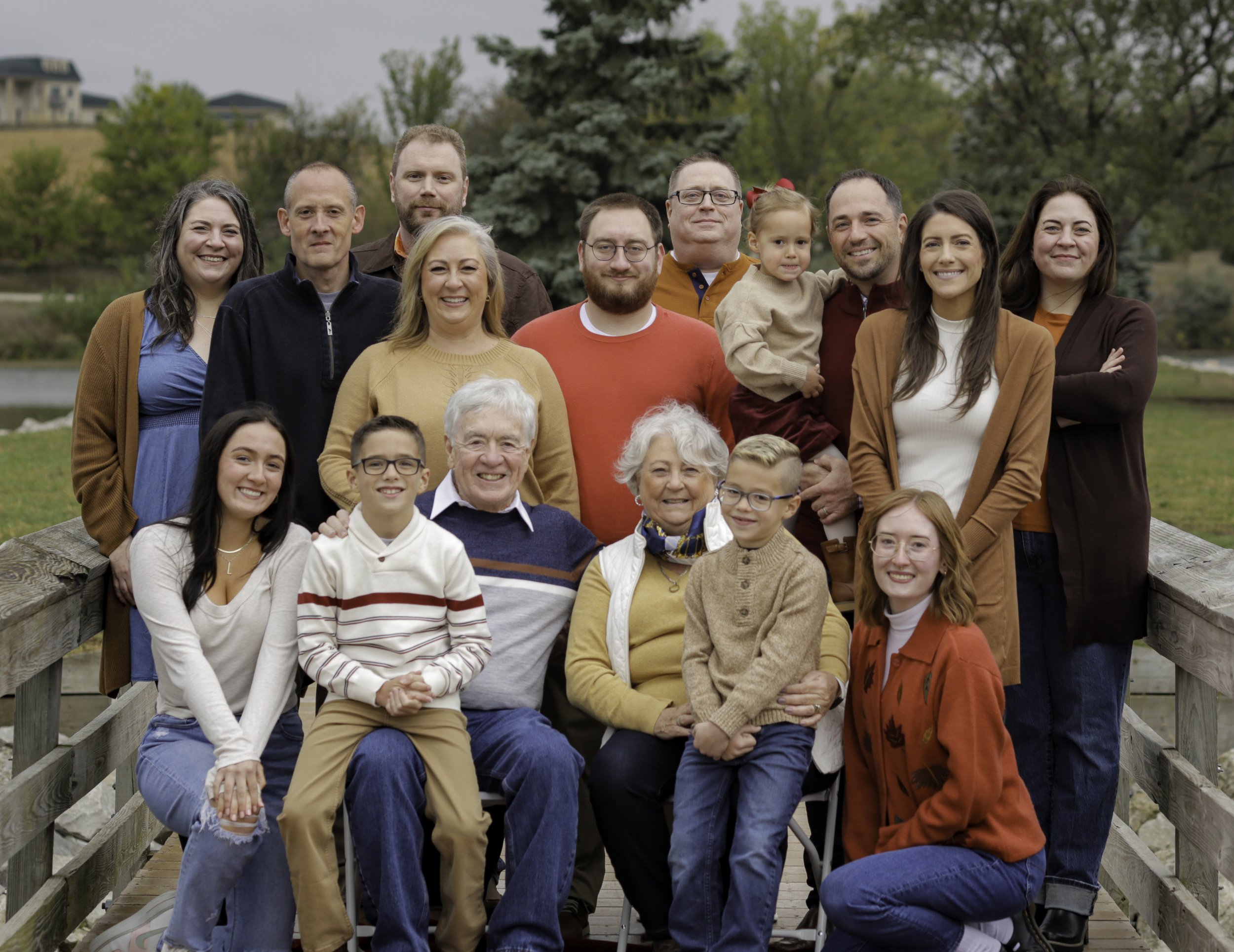 Family posing together on a wooden bridge in a park setting with trees and grass in the background.