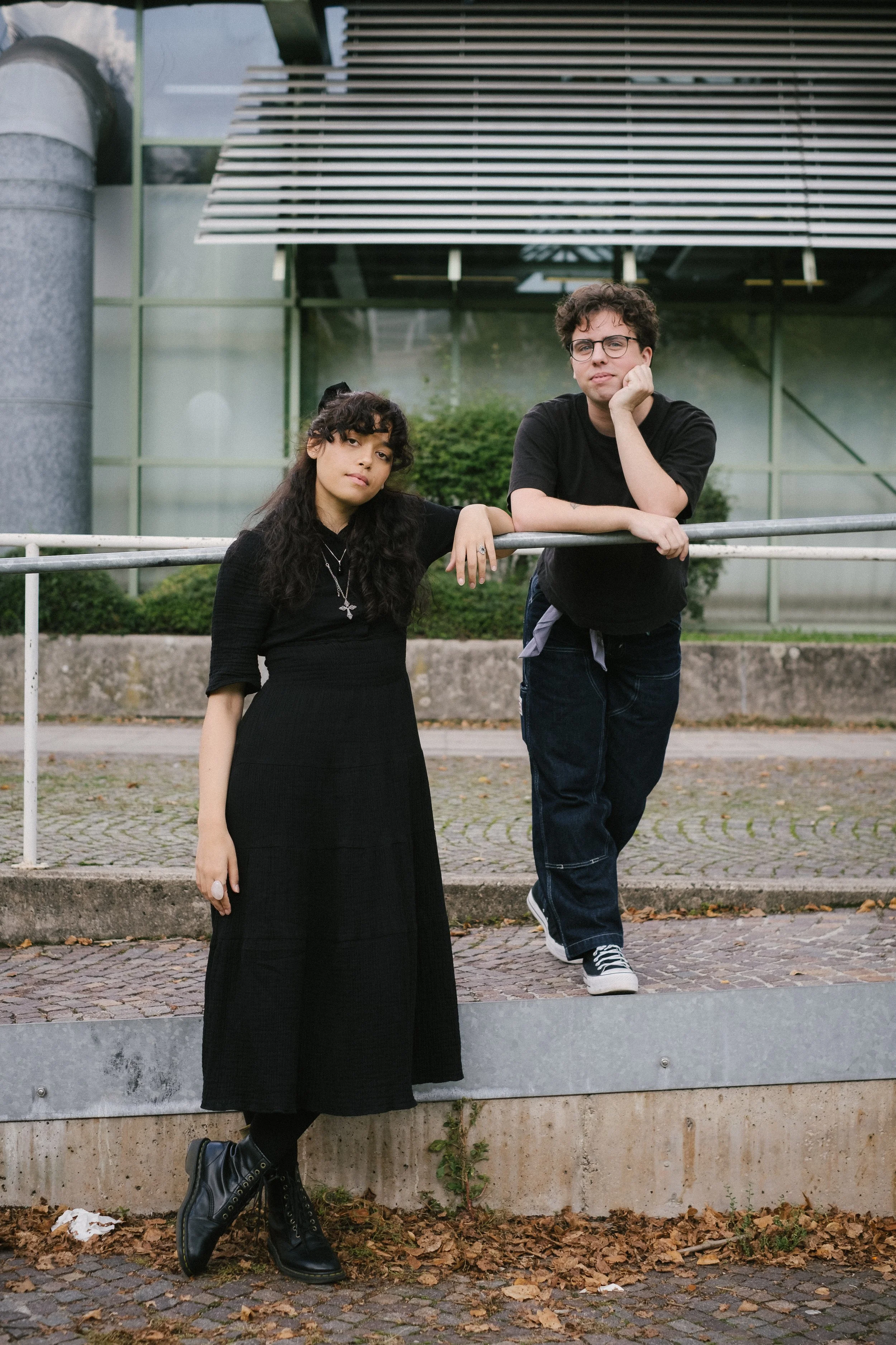 Franziska and Casey wearing black clothes leaning on a railing and looking into the camera.