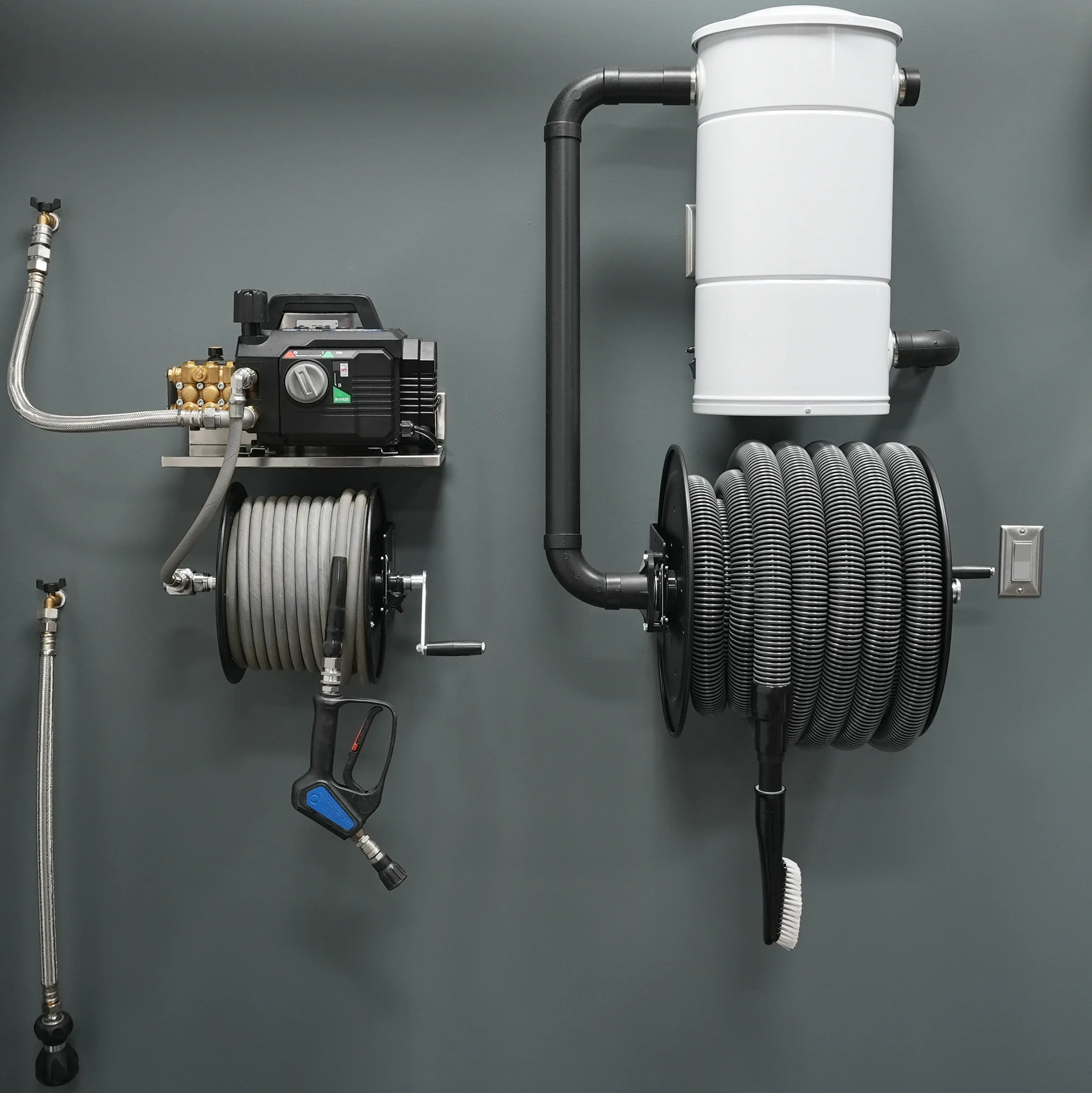 A wall-mounted vacuum system with hoses and a control unit, including a white cylindrical filter, black and metal pipes, and flexible hoses.