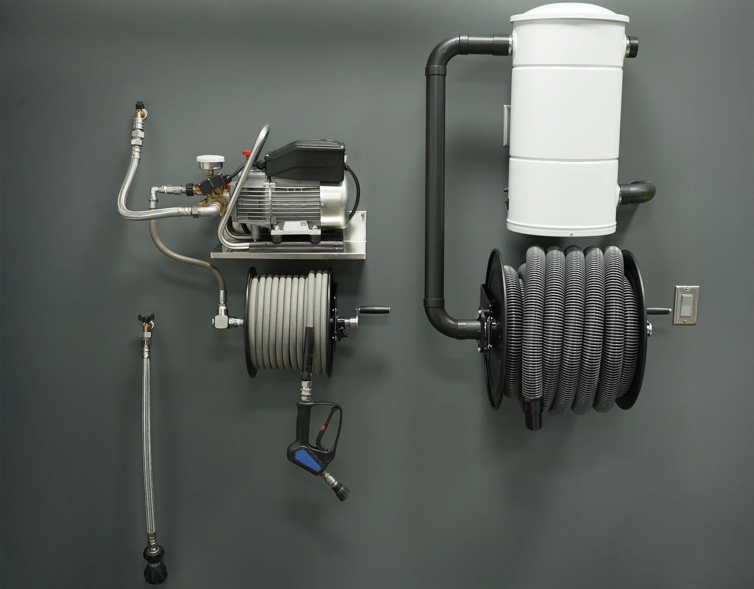 A vacuum pump system mounted on a gray wall, featuring various pipes, hoses, and a white filter or separator unit.