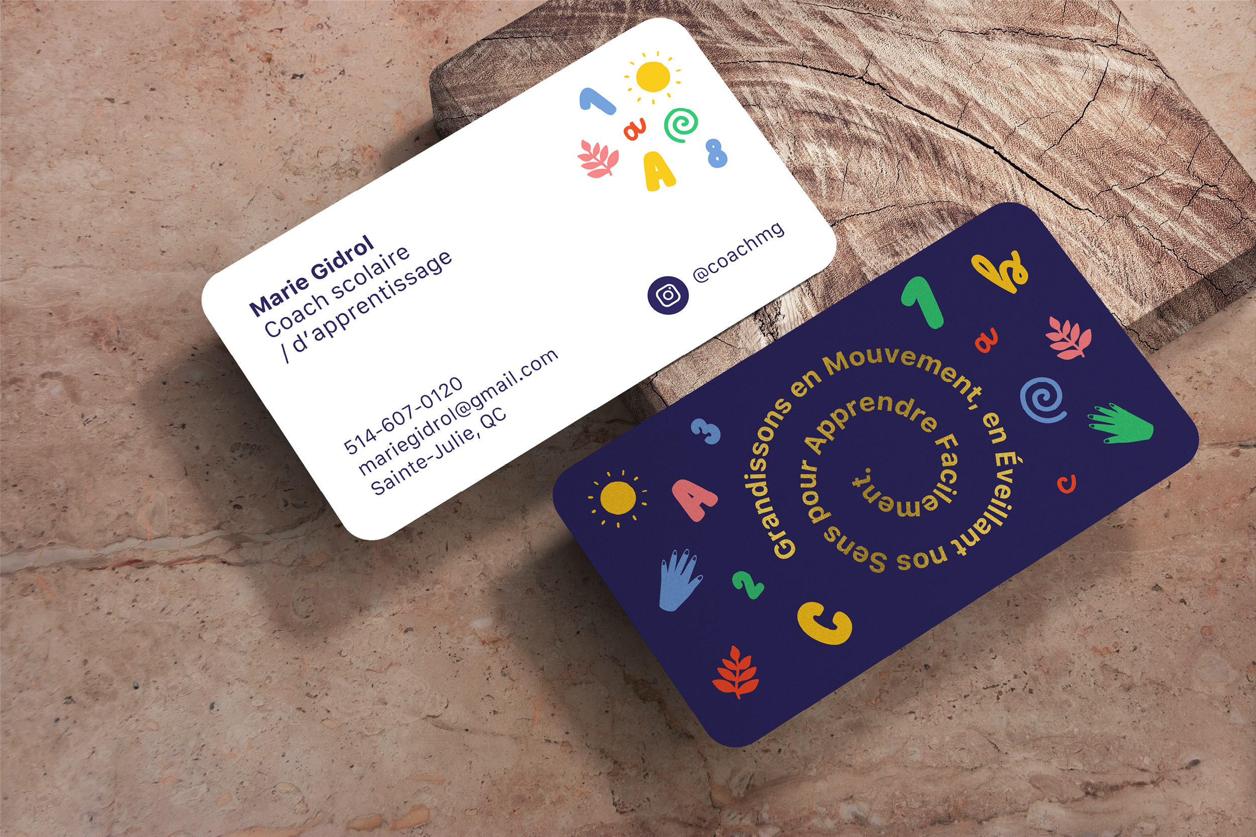Two colorful business cards for Marie Gidrol, a school coaching and learning expert, placed on a textured surface. The card features contact information, social media handle, and playful educational graphics. The reverse card displays a circular arra