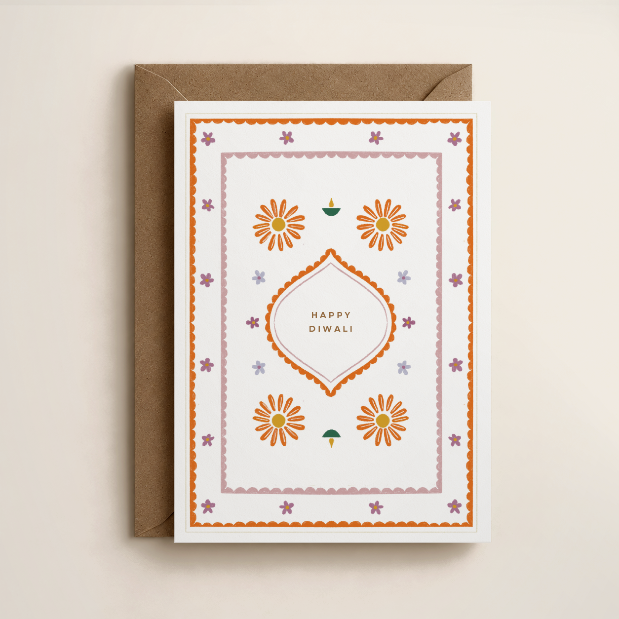 A Diwali greeting card with orange and purple floral designs, a diya lamp illustration, and 'Happy Diwali' printed in the center, placed on a brown envelope.