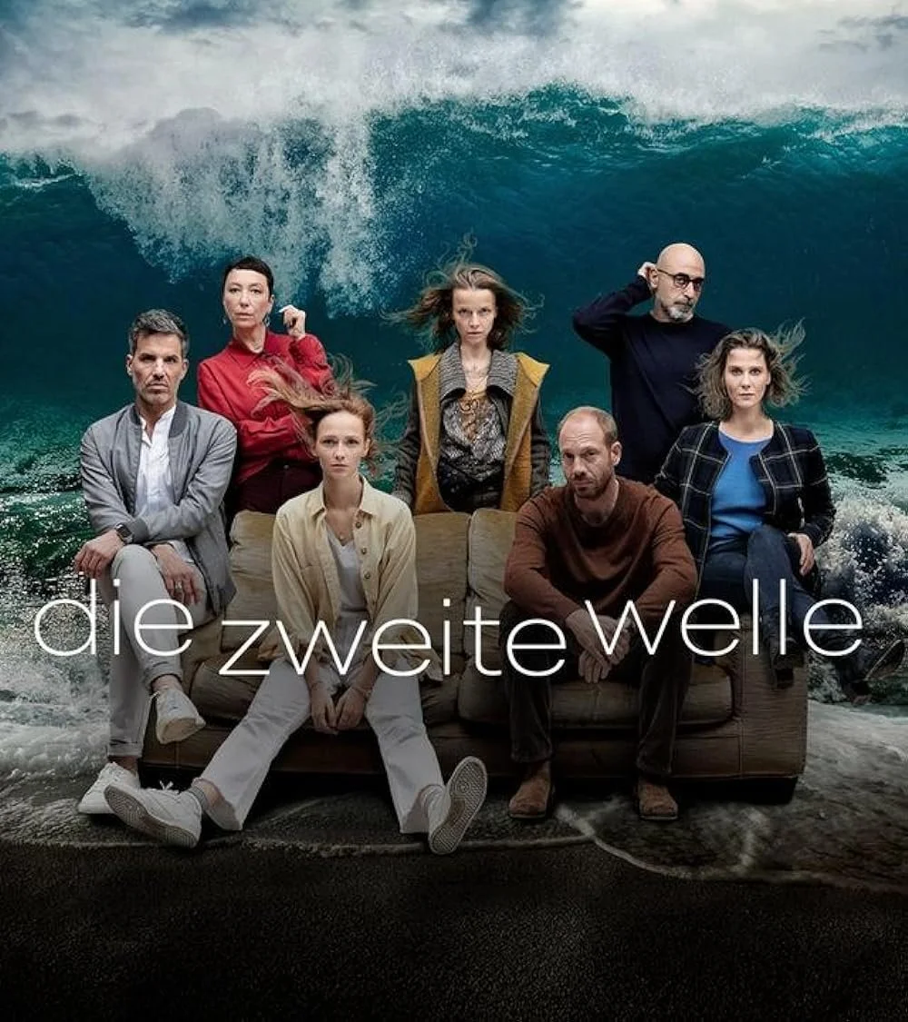 Gruppenshoot von sieben Menschen, sitzend auf einem Sofa vor einer riesigen Meereswelle im Hintergrund, mit dem Titel 'die zweite welle'.