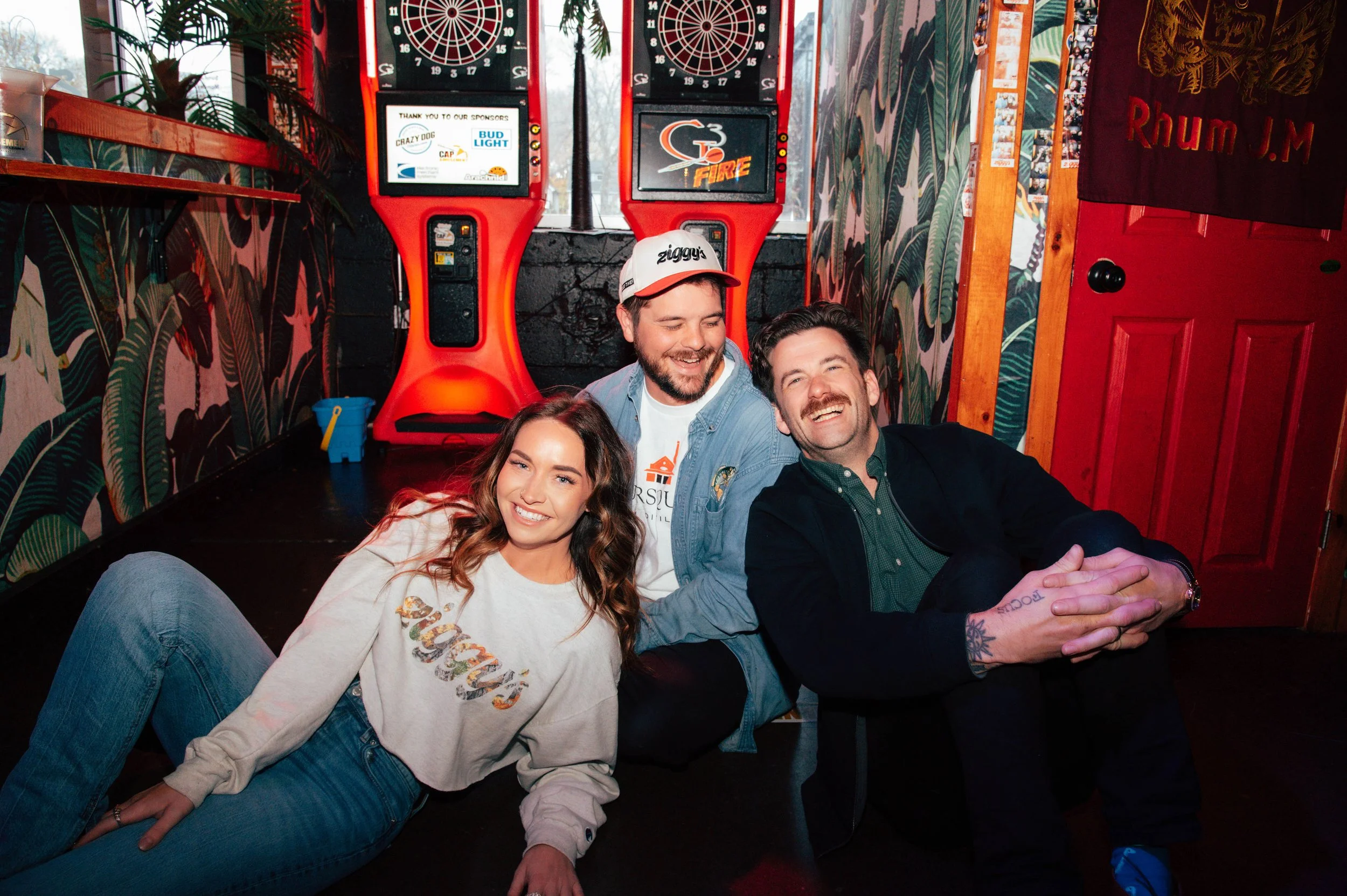 Friends hanging out at Ziggy’s neighborhood bar in Rochester, NY, sitting by dartboards and bar games, smiling and enjoying the lively atmosphere.
