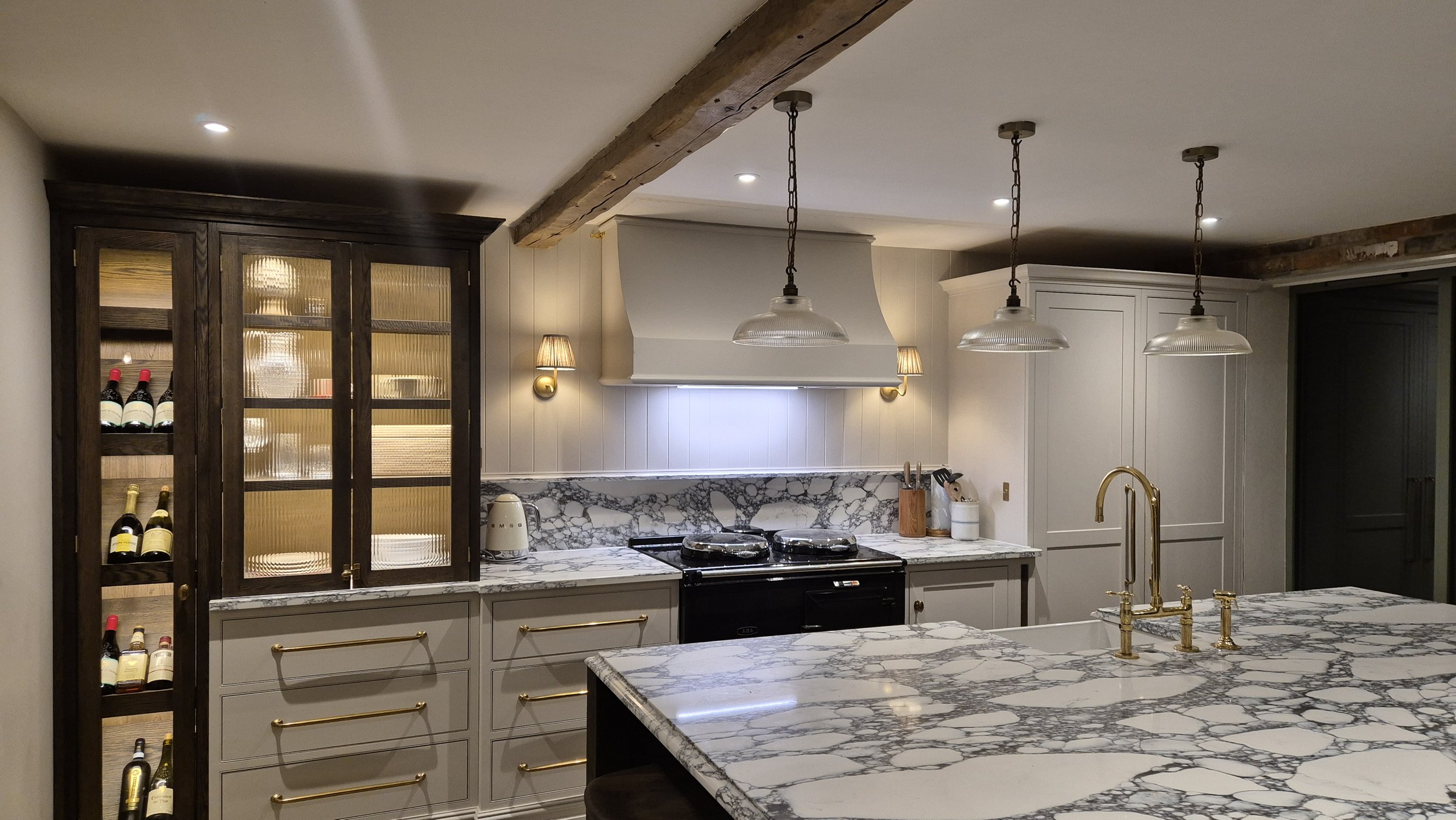 Modern kitchen with a marble island, gold fixtures, a wine cabinet, and a stove with overhead lighting