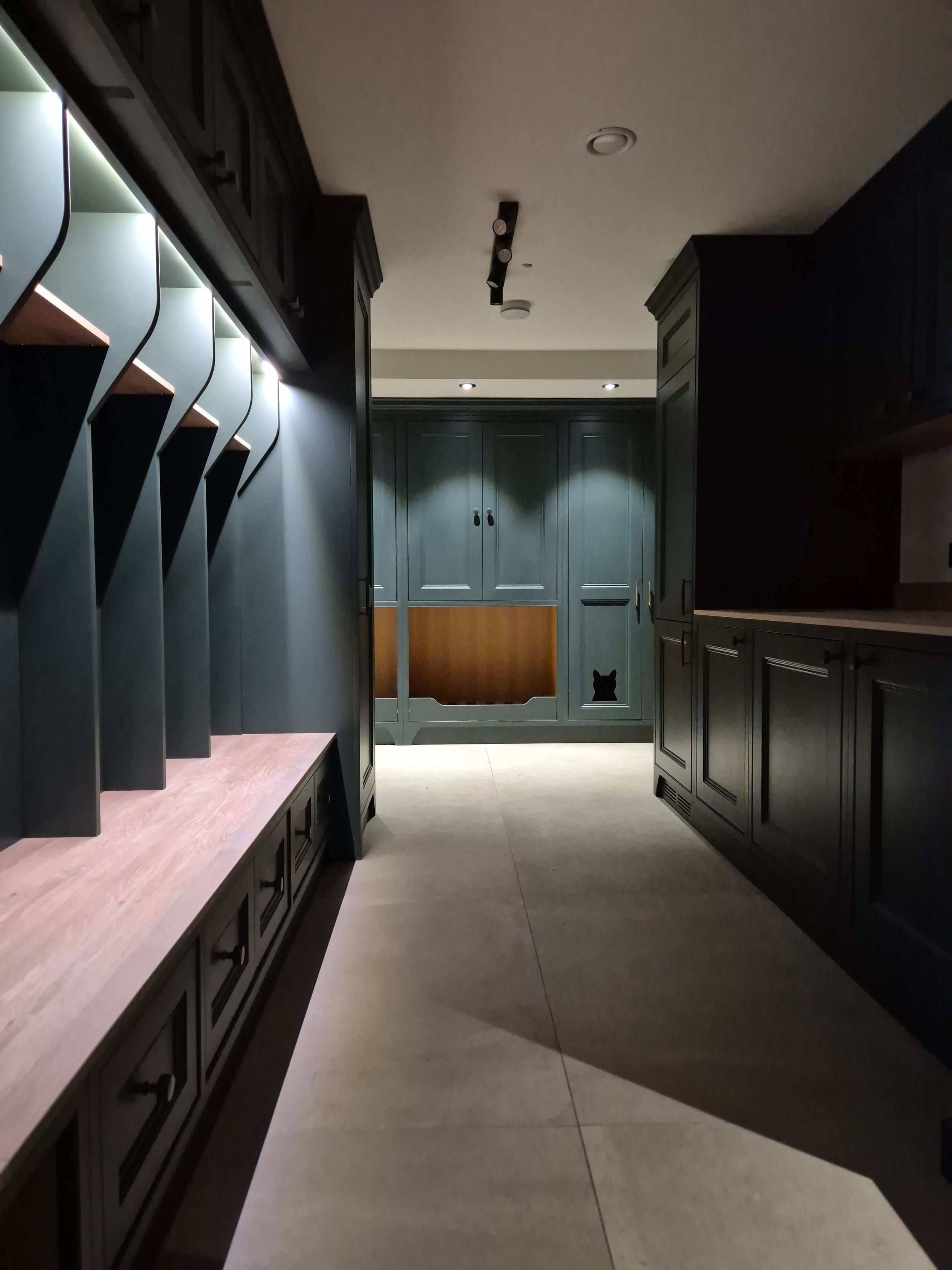 Dimly lit hallway or kitchen with black cabinetry, a wooden countertop, and a decorative cutout of a black cat silhouette on the cabinet door at the end.