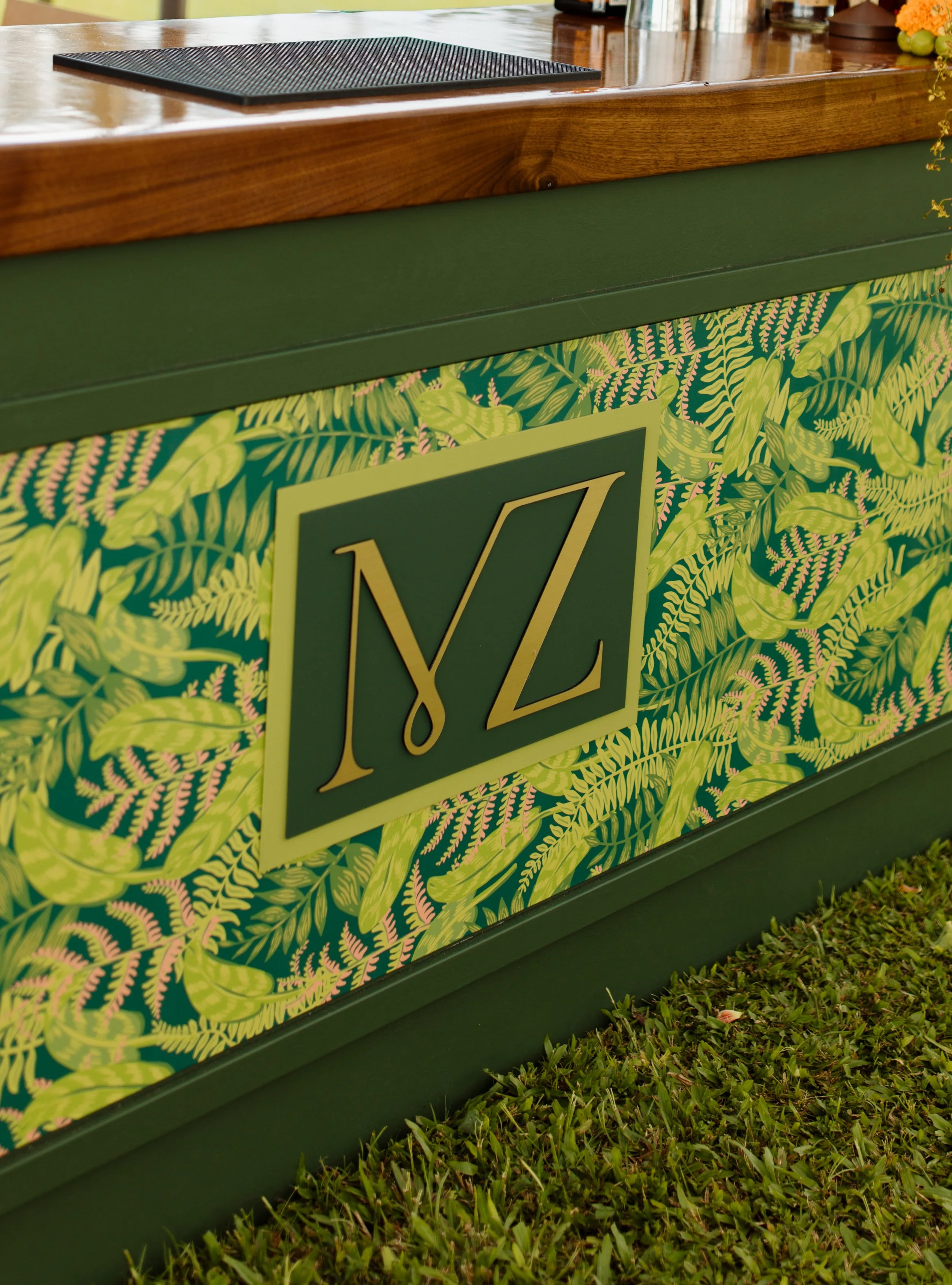 Close-up of a decorated bar or counter with a green leafy pattern and a large plant emblem, topped with a wooden surface.