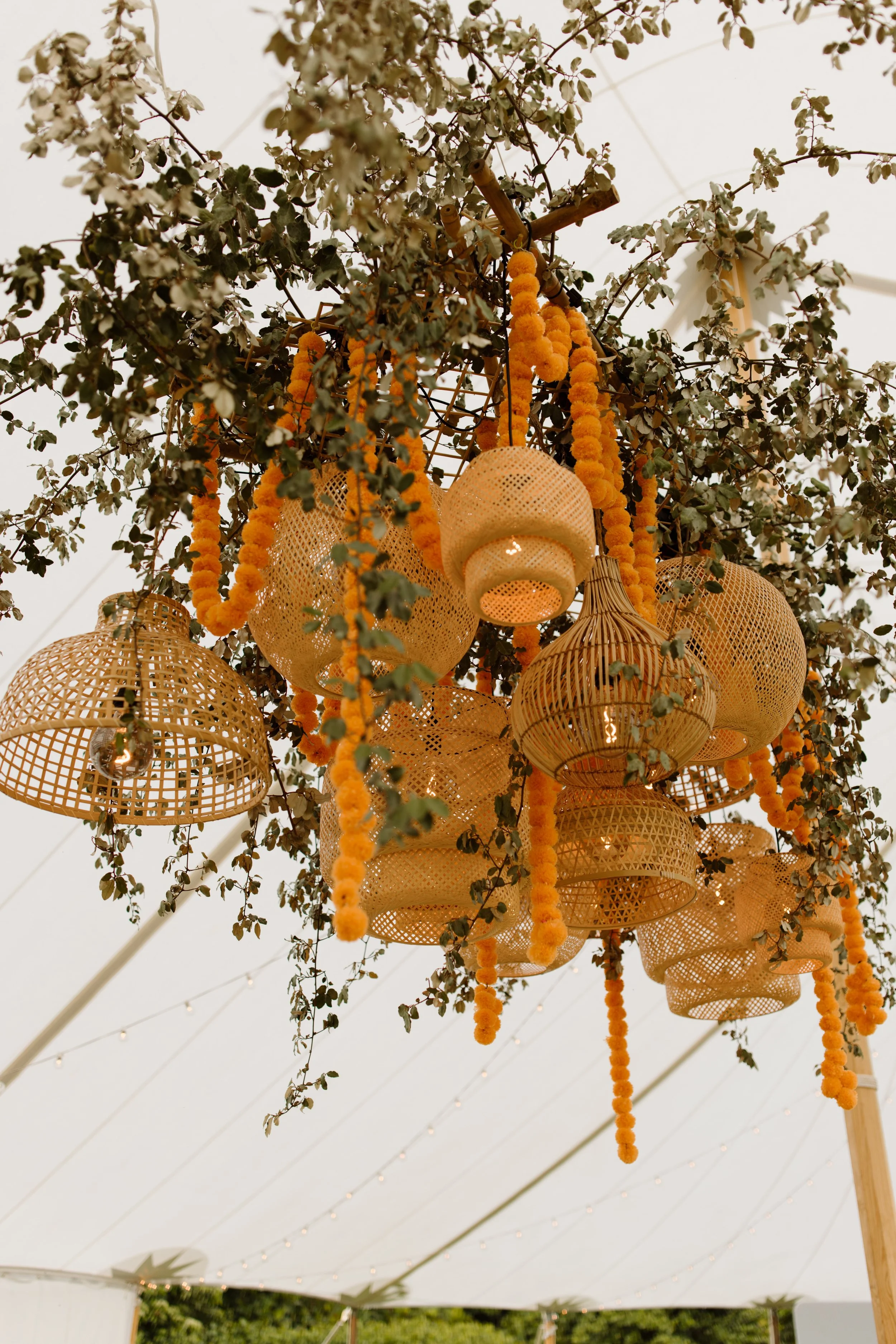 Decorative hanging lanterns and garlands of orange marigold flowers hanging from a canopy, with string lights in the background.