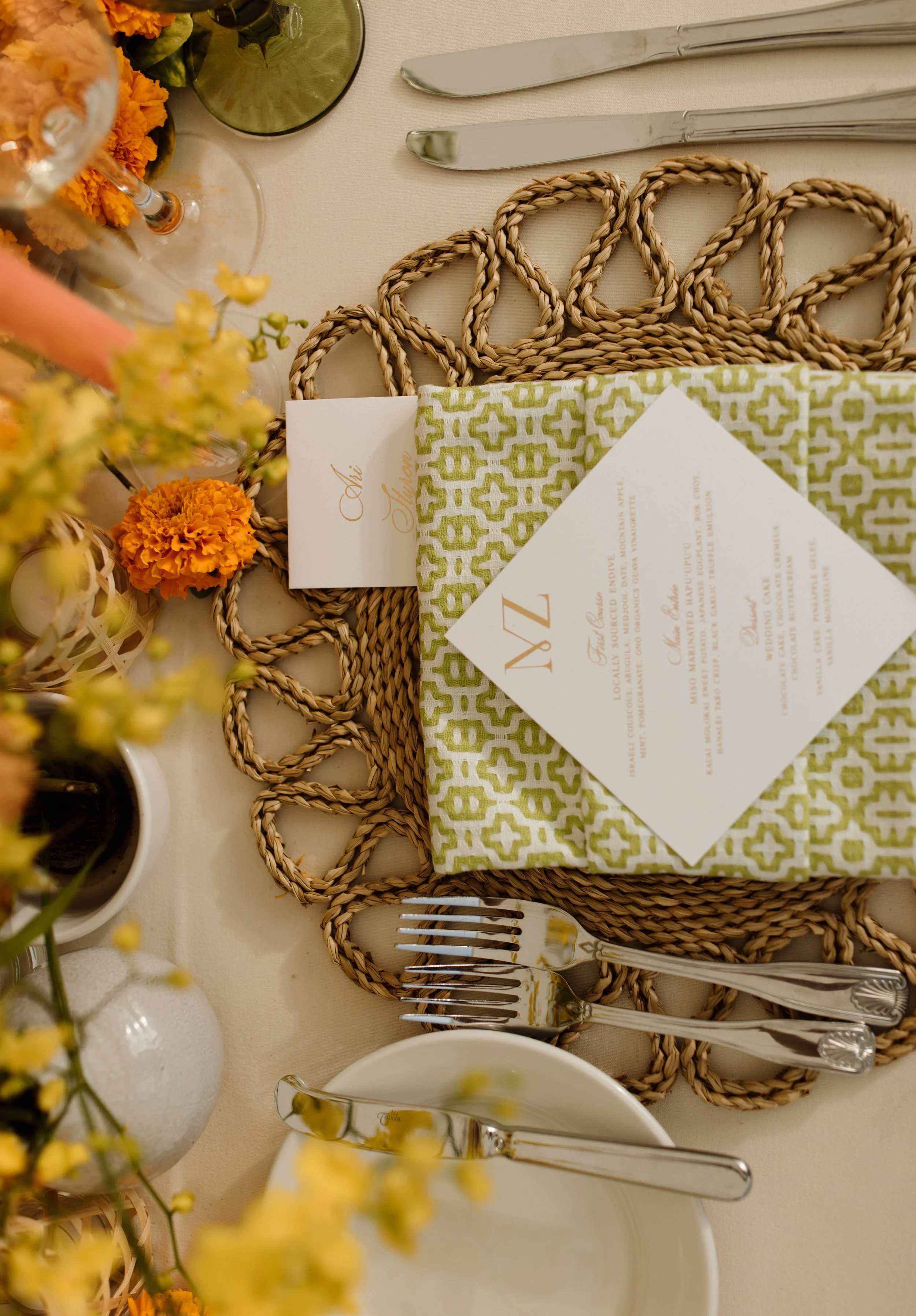 A neatly set table with a woven placemat, silverware, a menu, and flowers.
