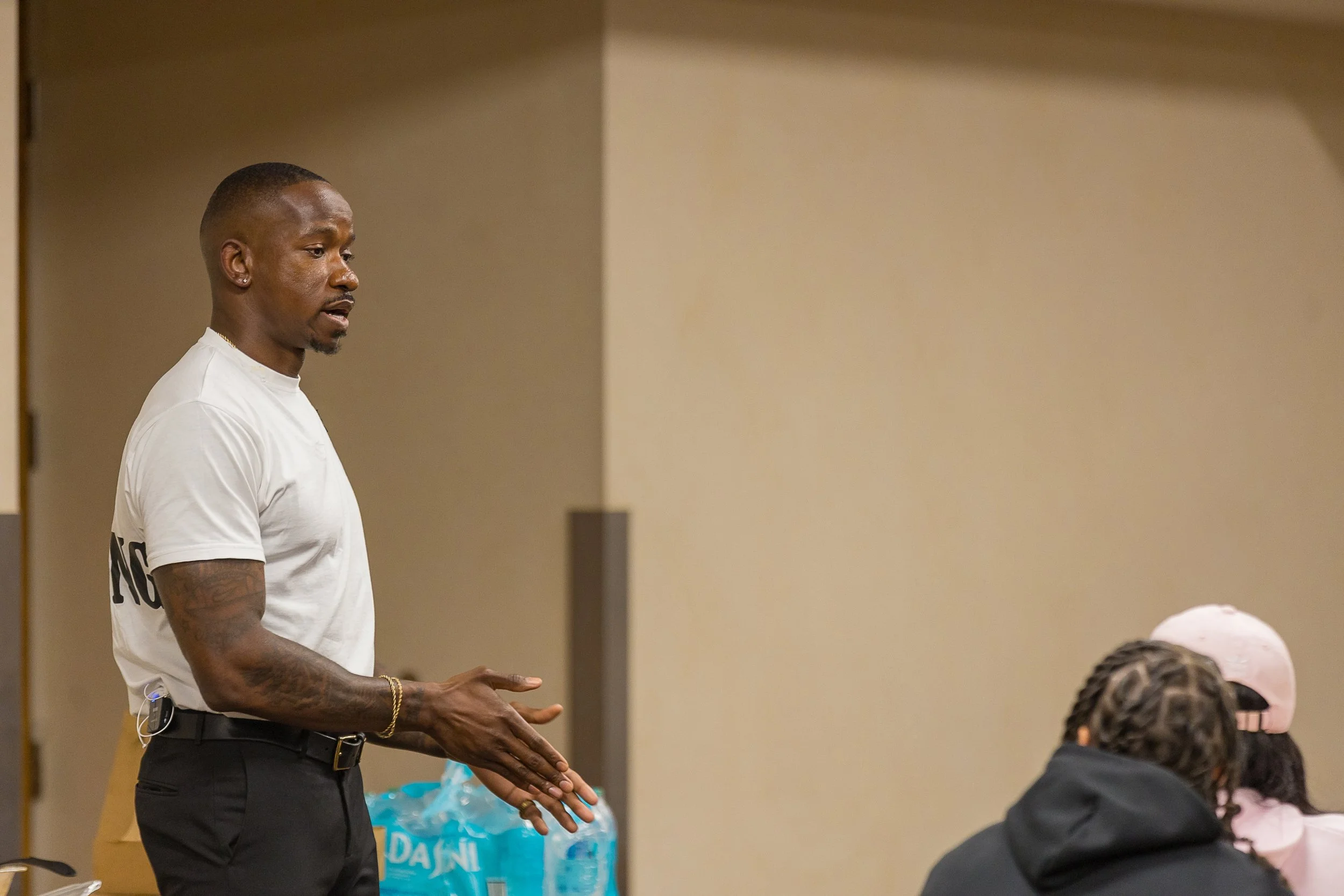 “Charleston Girley speaking to a group during an indoor event, wearing a white shirt and black pants.”