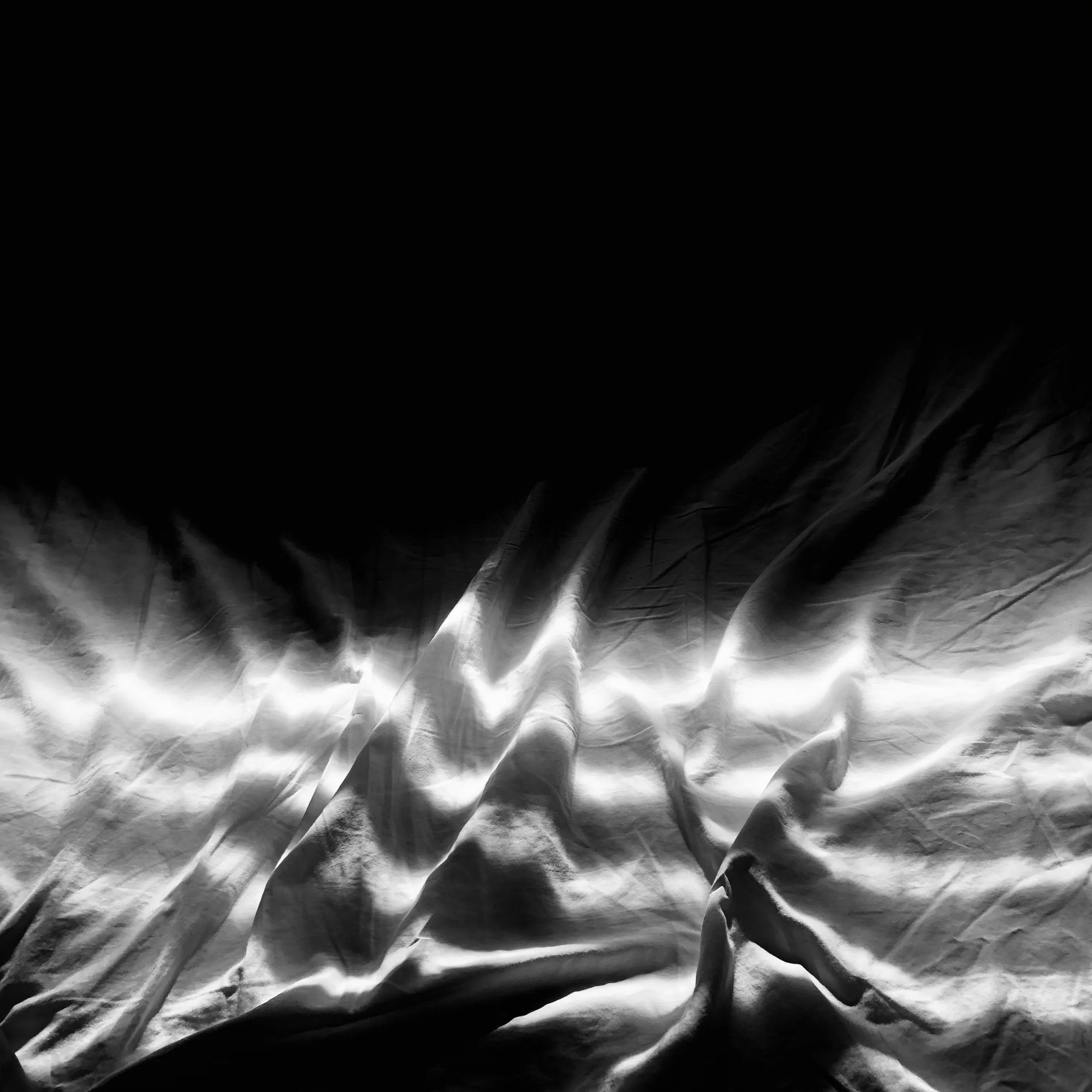 Close-up of crumpled white fabric with light and shadow creating a textured pattern.