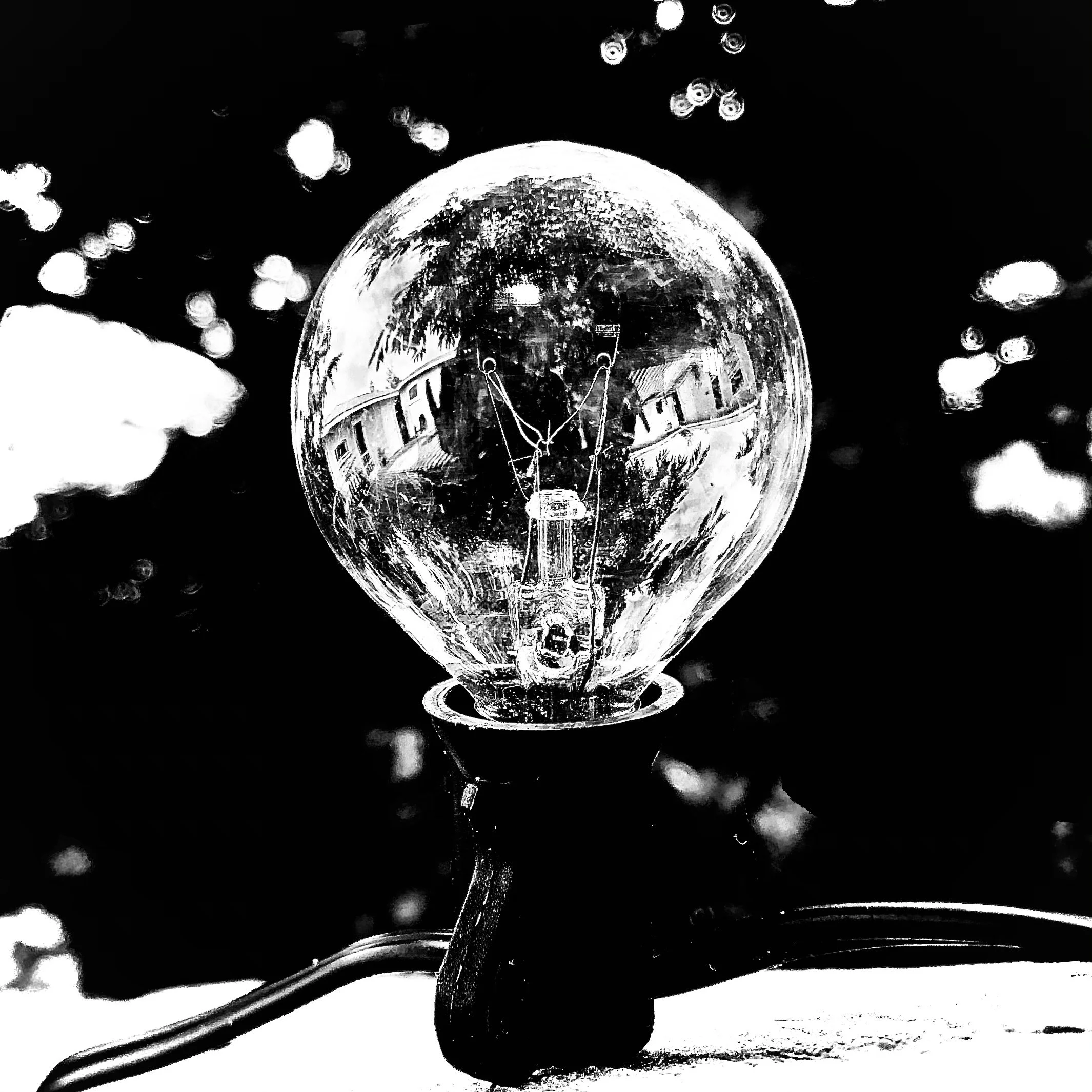 A black and white photo of a light bulb with a reflection of houses and trees in the glass.