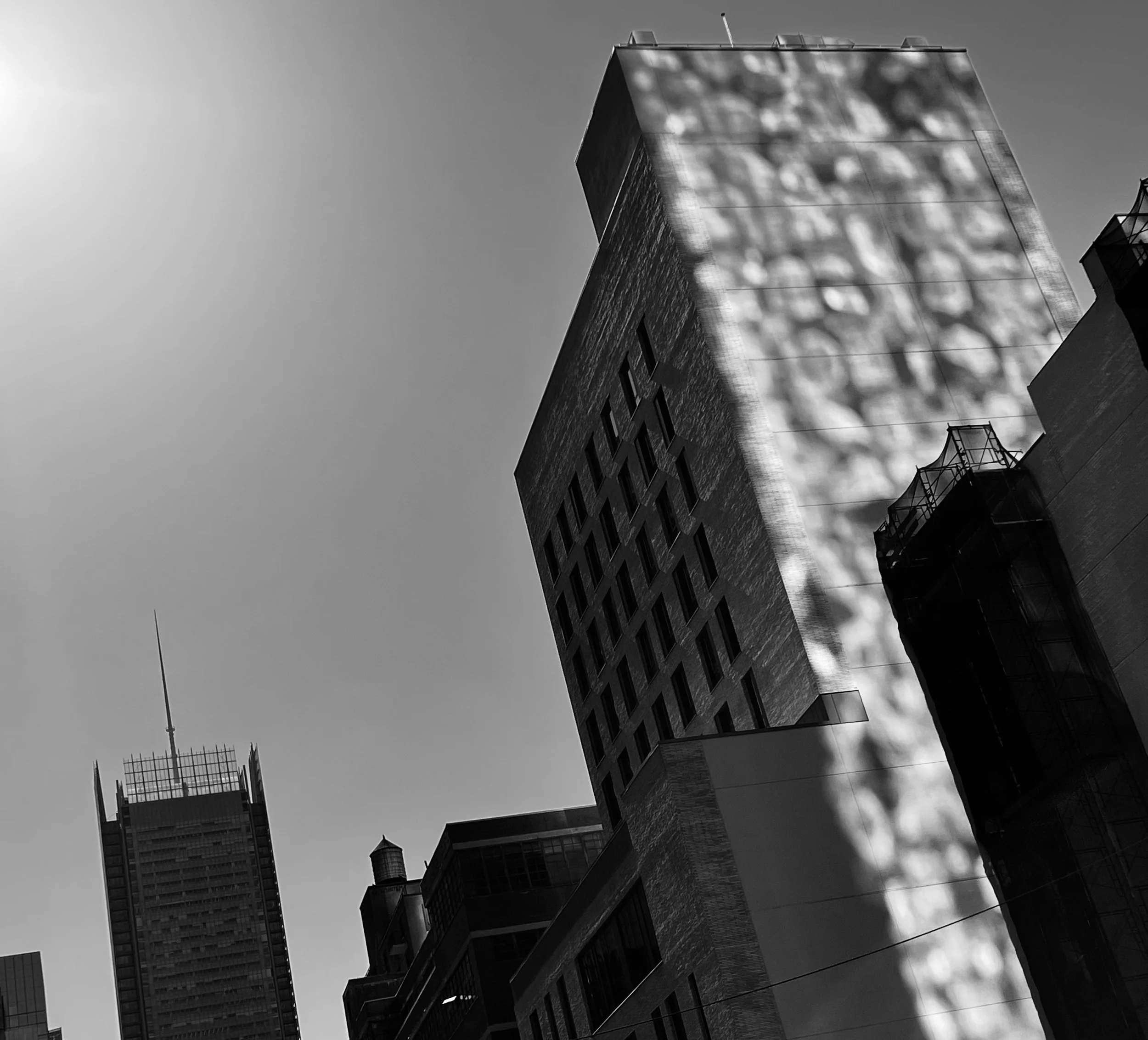 Black and white photo of tall modern city buildings with shadows and reflections on the facade, taken from a low angle against a clear sky.