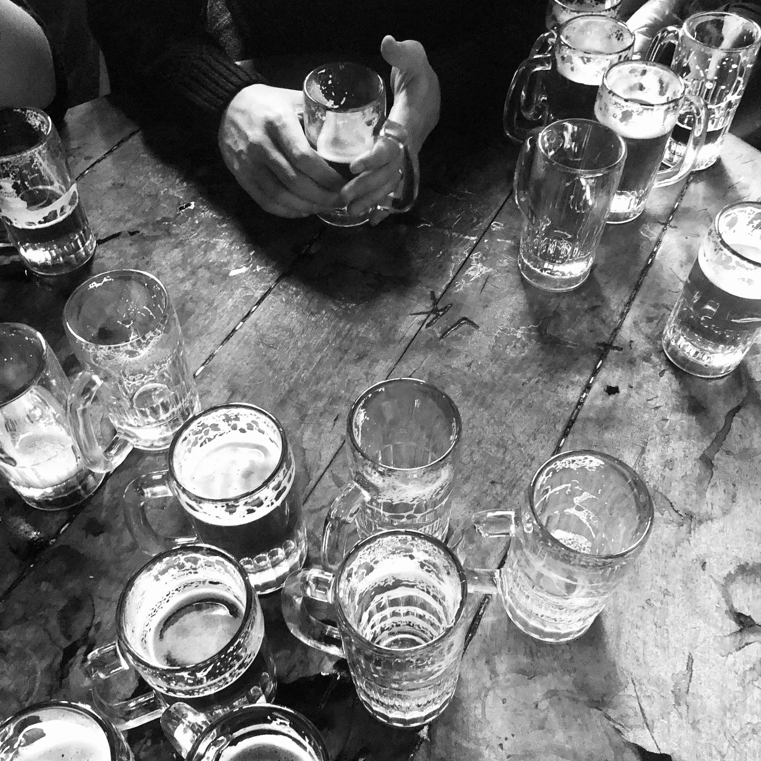 Several glasses of beer on a wooden table with a person's hand holding a glass, in black and white.