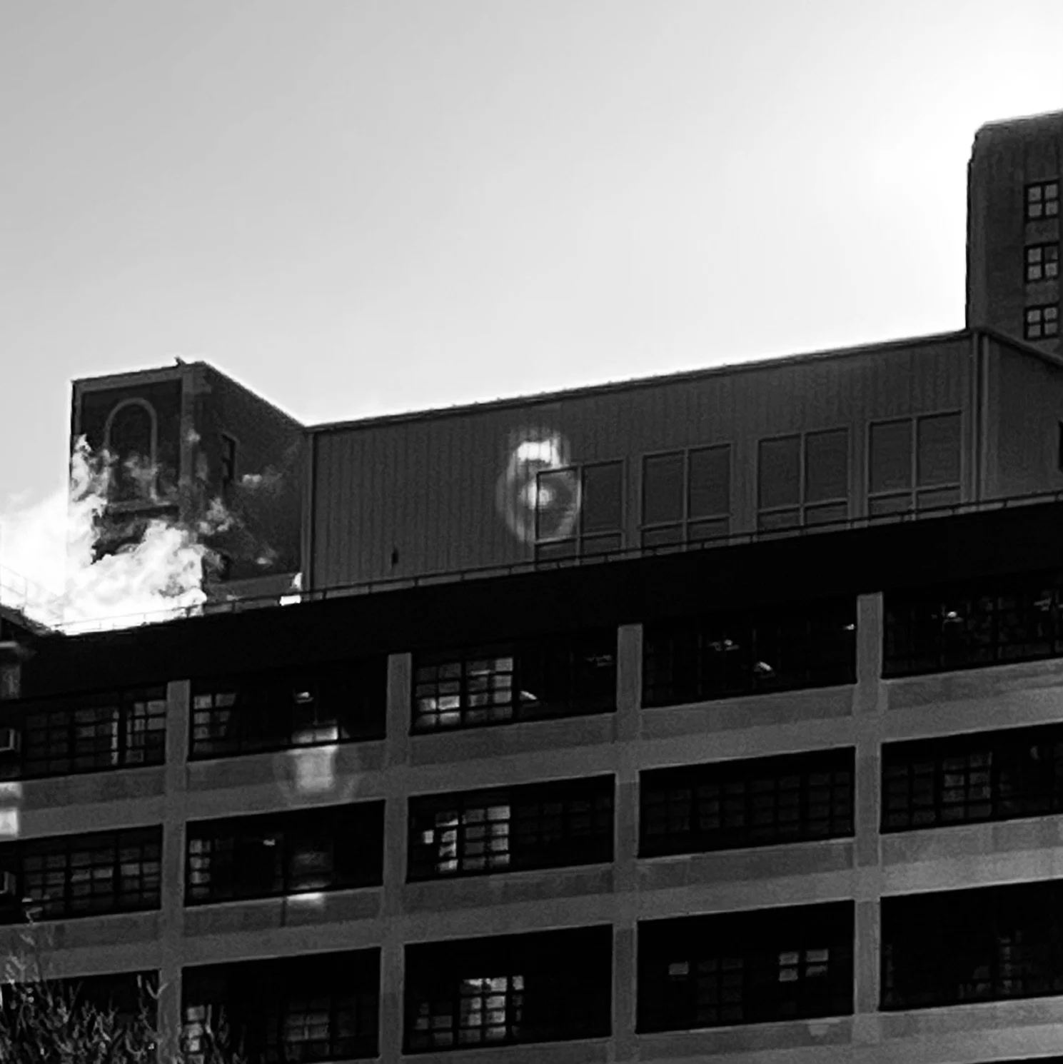 Black and white photo of a multi-story parking garage with an office building on top, a satellite dish, and a large screen on the building's facade.