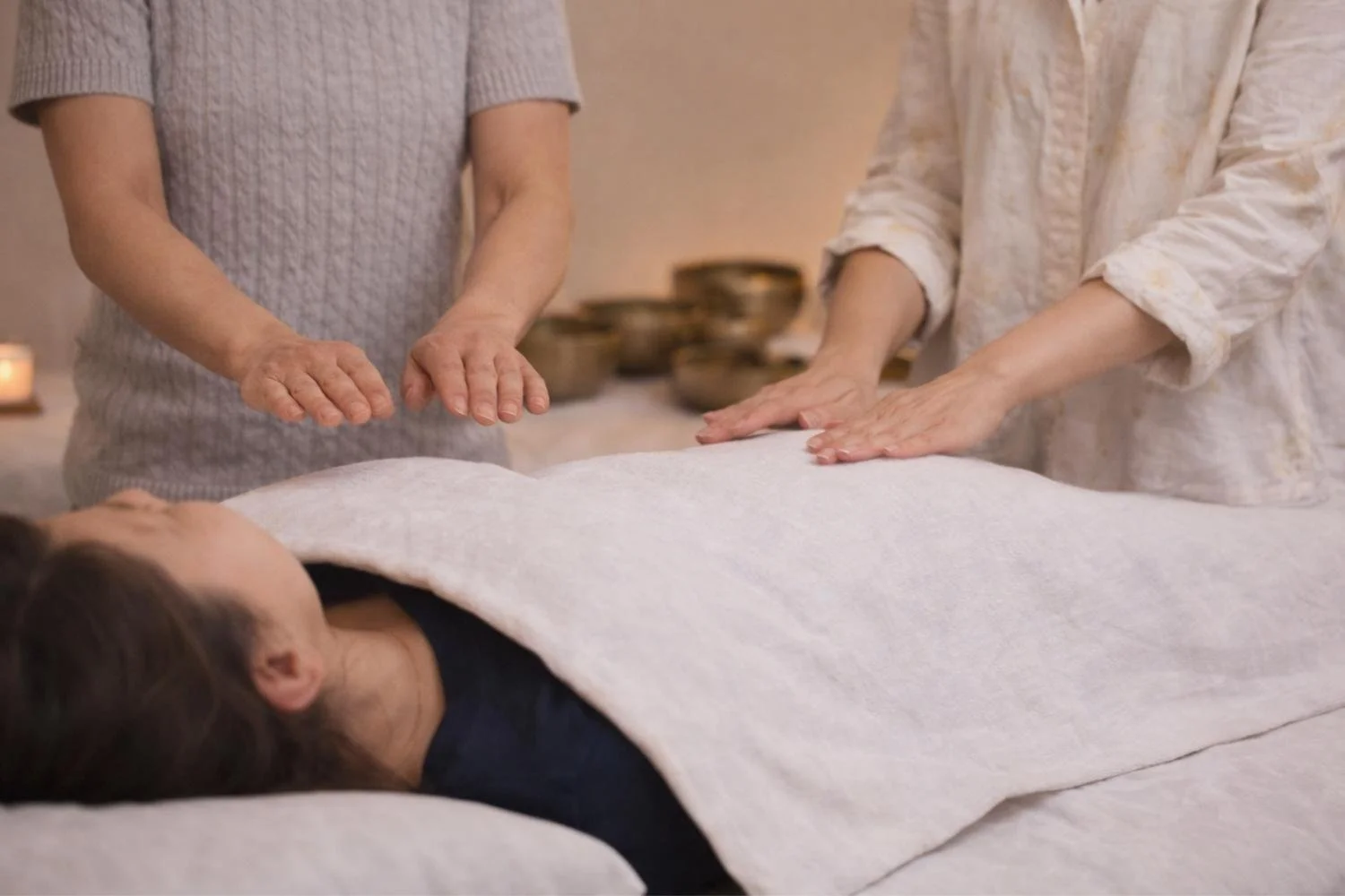 People giving a massage or healing treatment to a woman lying on a table, covered with a blanket.
