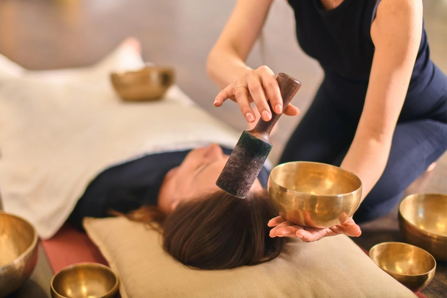 Person receiving a sound healing or sound therapy treatment with brass singing bowls and a mallet.