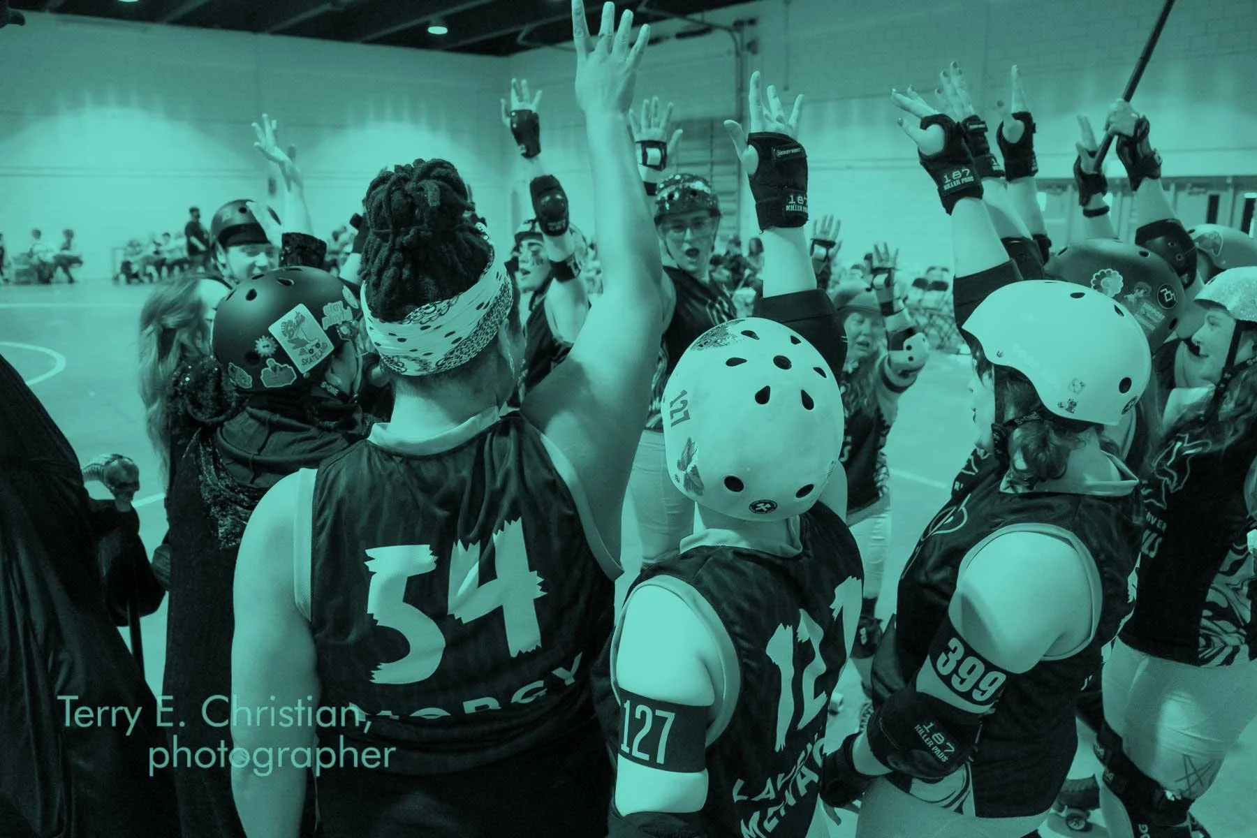 Roller derby team in a roller rink, gathered in a huddle, wearing helmets and protective gear.