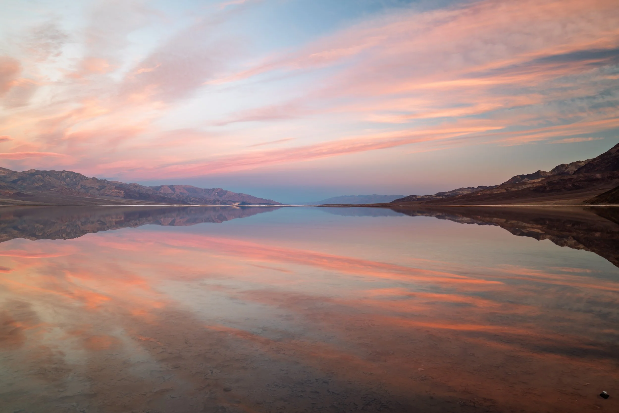 Mirror World
Lake Manly appears as a thin, impossible sheet of water spread across the salt flats of Badwater Basin, turning the lowest point in North America into a vast mirror. Mountains stretch upside‑down across its surface, clouds drift in it as