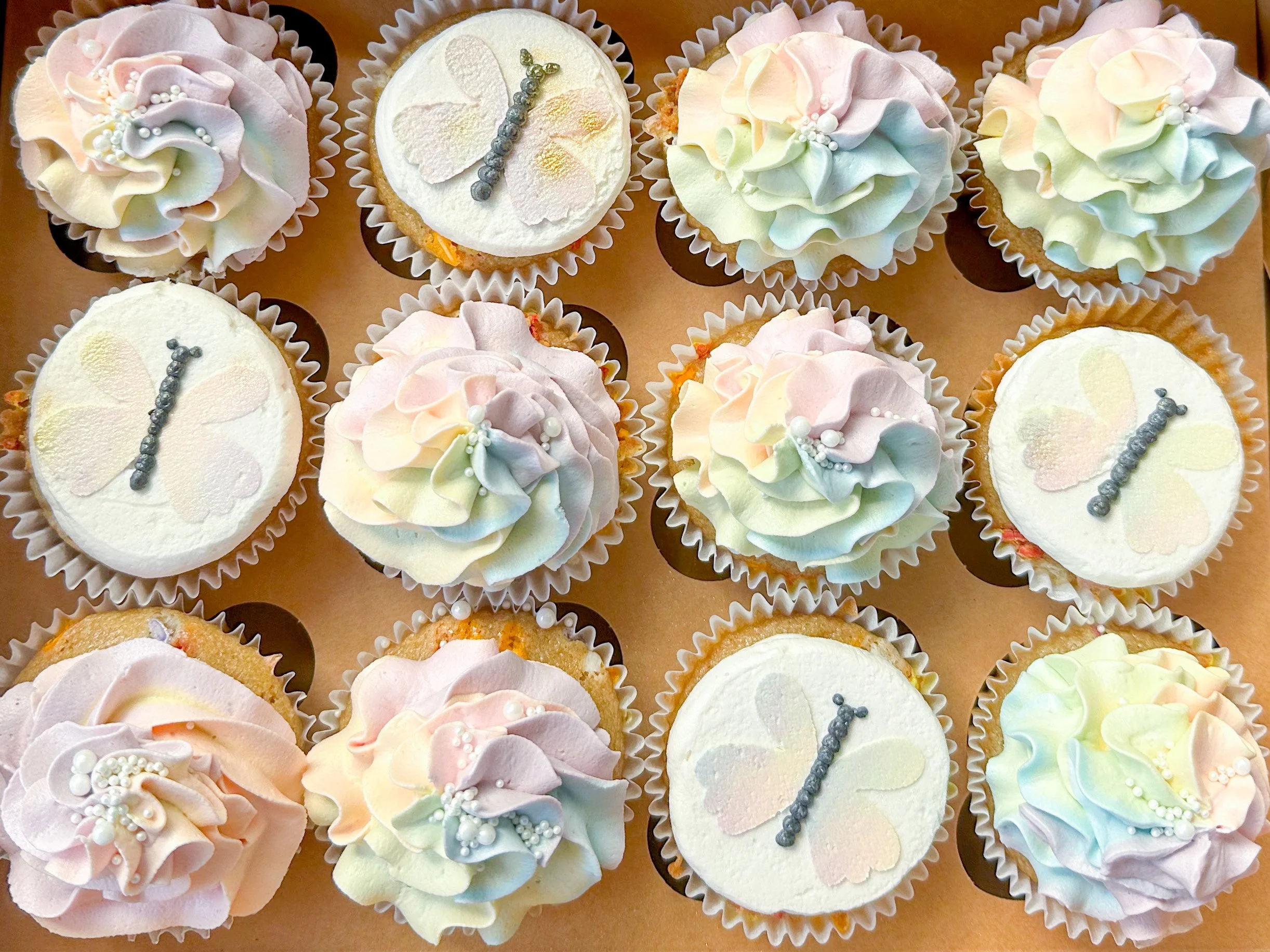 A box of cupcakes with pastel-colored frosting and butterfly decorations.