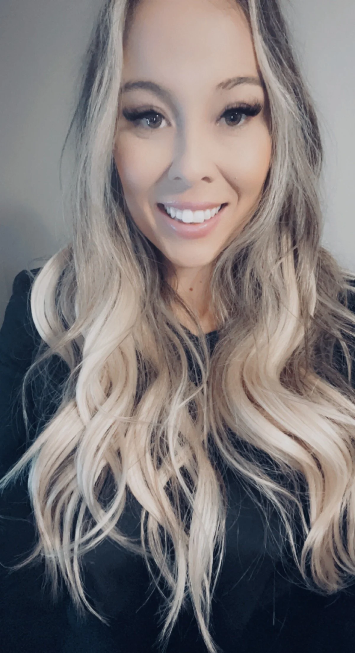 A smiling woman with long, wavy blonde hair and makeup.
