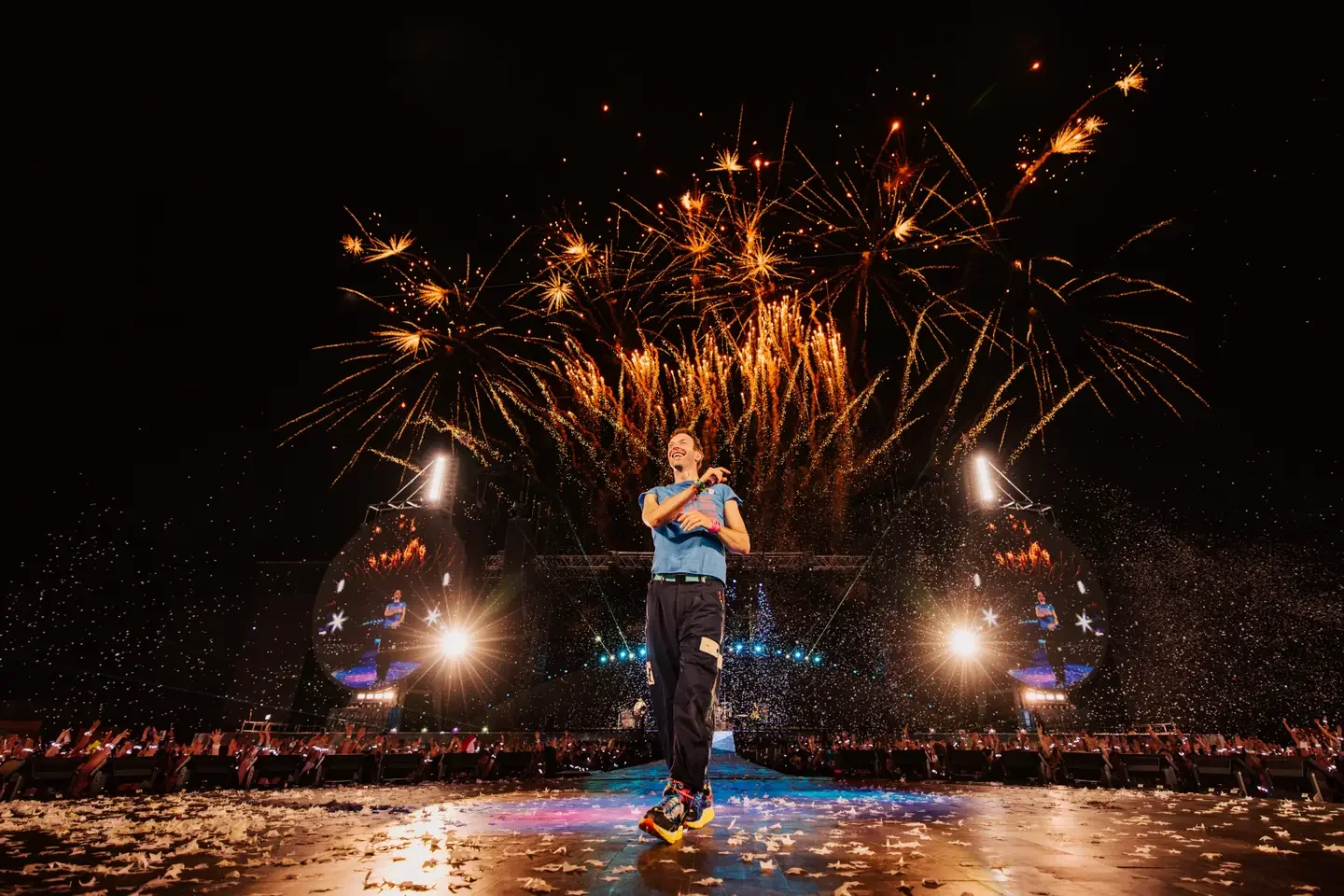 Performer on stage with fireworks overhead during a concert or celebration.