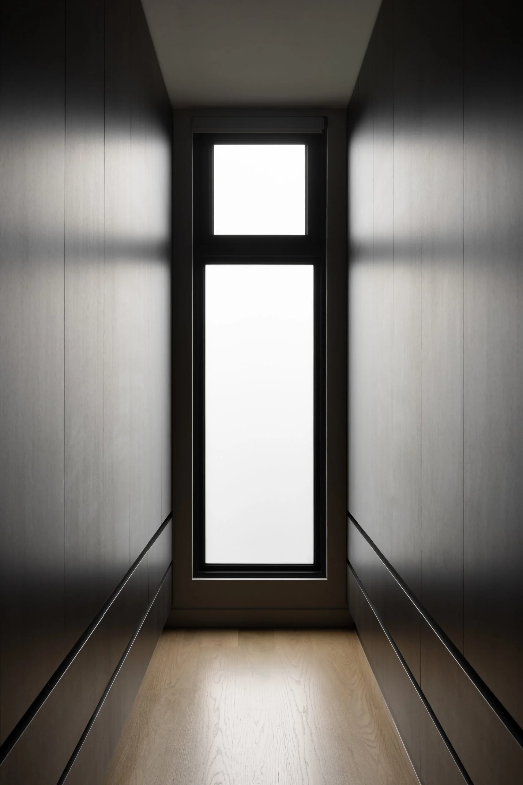 Contemporary Melbourne apartment walk-in wardrobe featuring full-height black joinery and a central window, demonstrating thoughtful planning and refined detailing.