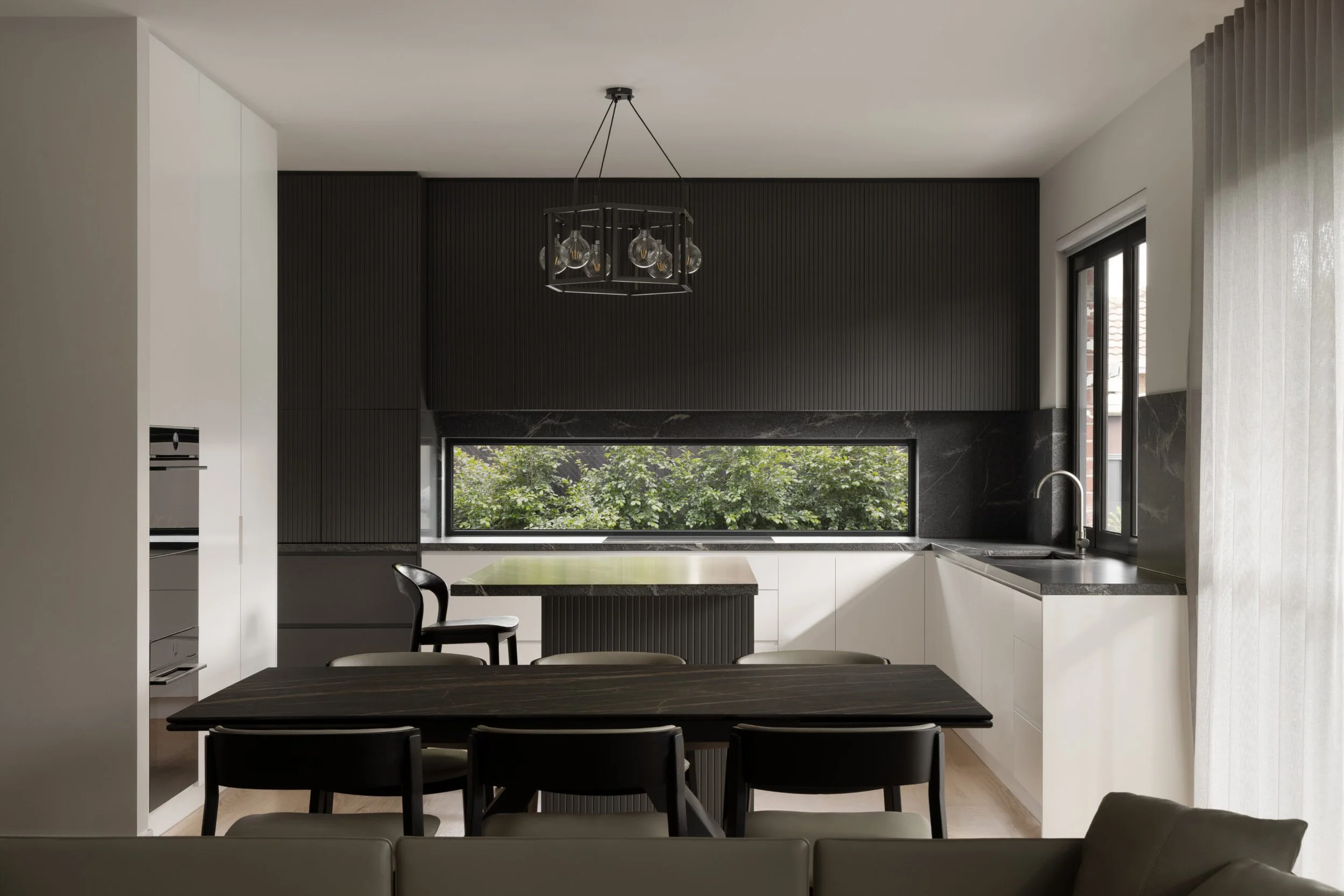 Contemporary Melbourne apartment kitchen with fluted black joinery, black stone surfaces and a picture window framing greenery. Thoughtful space planning balances functionality with a refined, cohesive aesthetic.