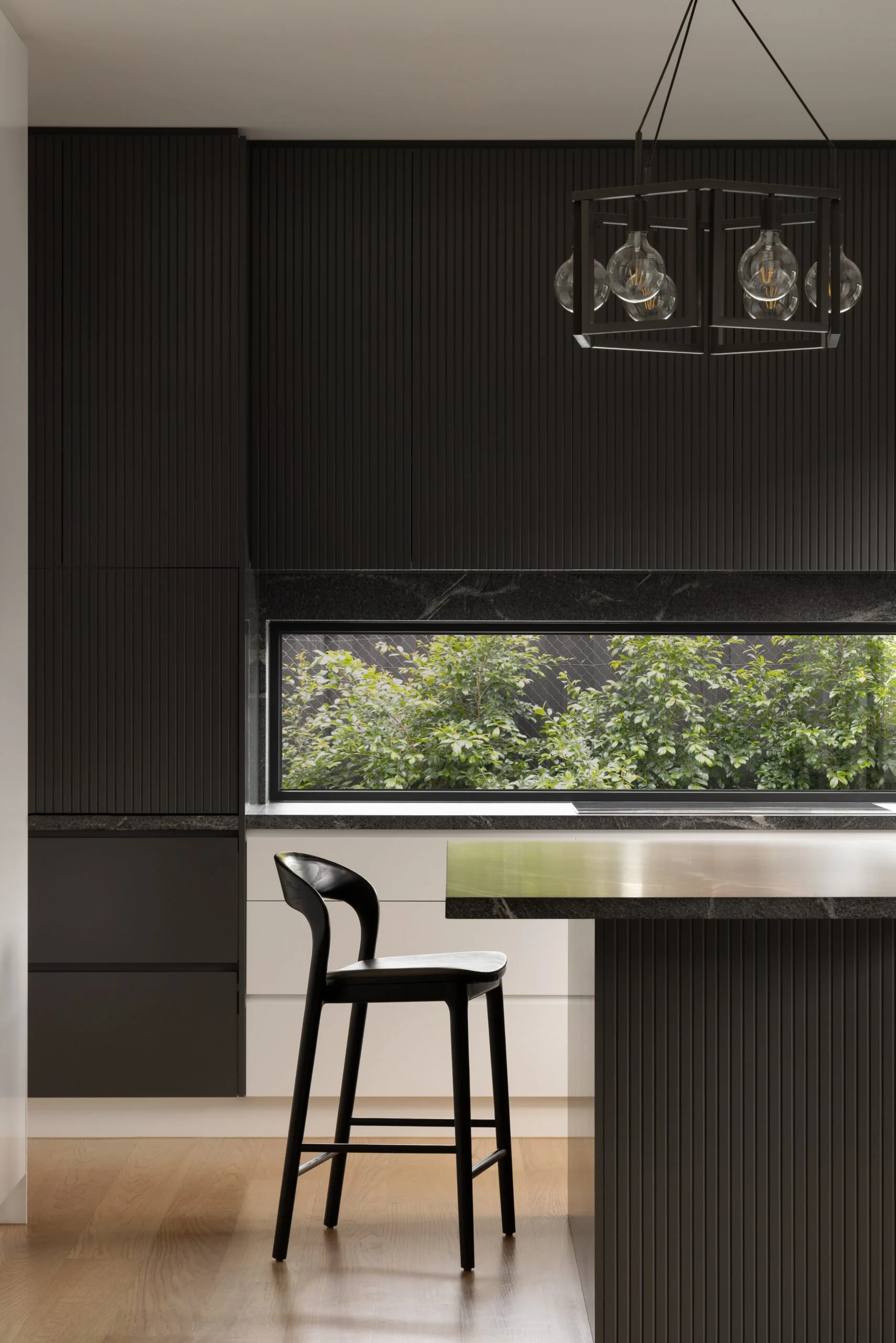 A contemporary Melbourne apartment kitchen, featuring fluted dark joinery, dark stone benchtops and integrated storage solutions.