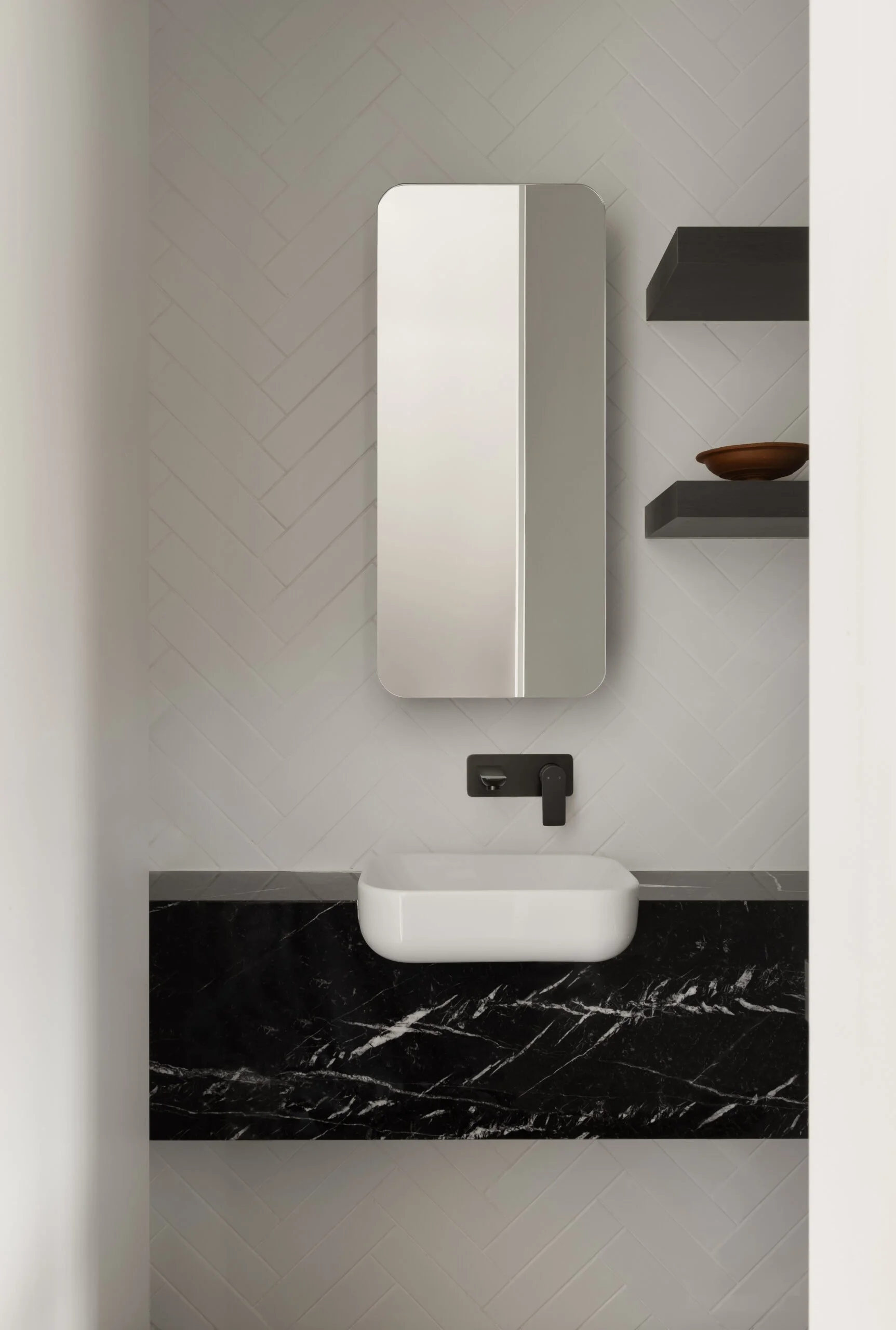 Contemporary Melbourne apartment powder room featuring a floating black stone vanity, herringbone wall tiles and a restrained material palette with refined detailing.