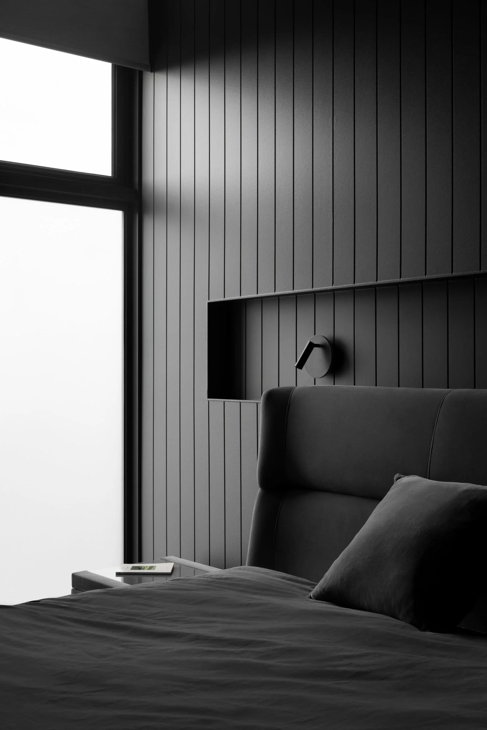 Contemporary Melbourne apartment bedroom featuring black VJ wall panelling, an integrated niche and upholstered bedhead, where texture brings warmth to a restrained palette.