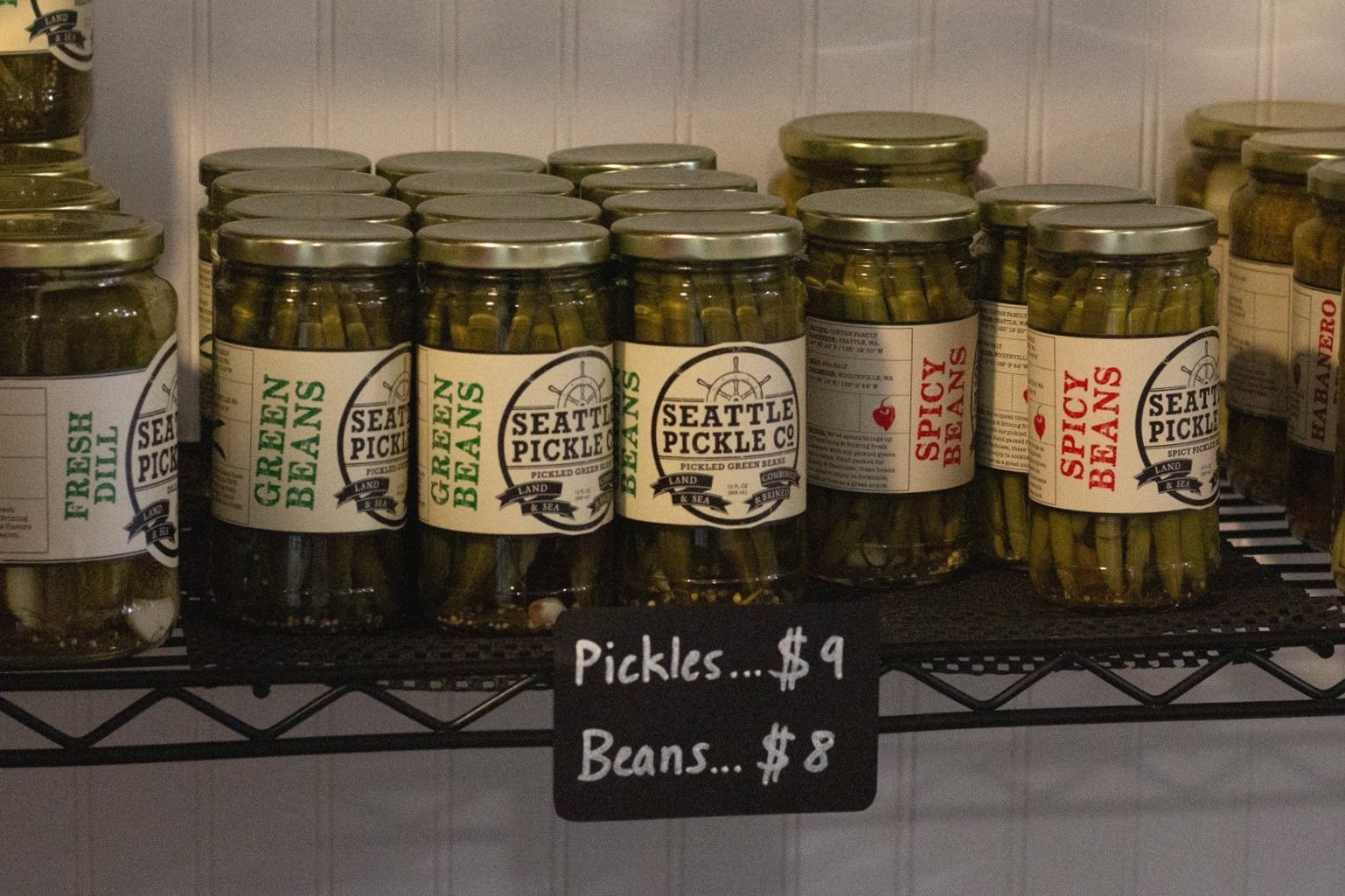 Pickle jars lined up with a sign that reads Pickles nine dollars, Beans eight dollars.