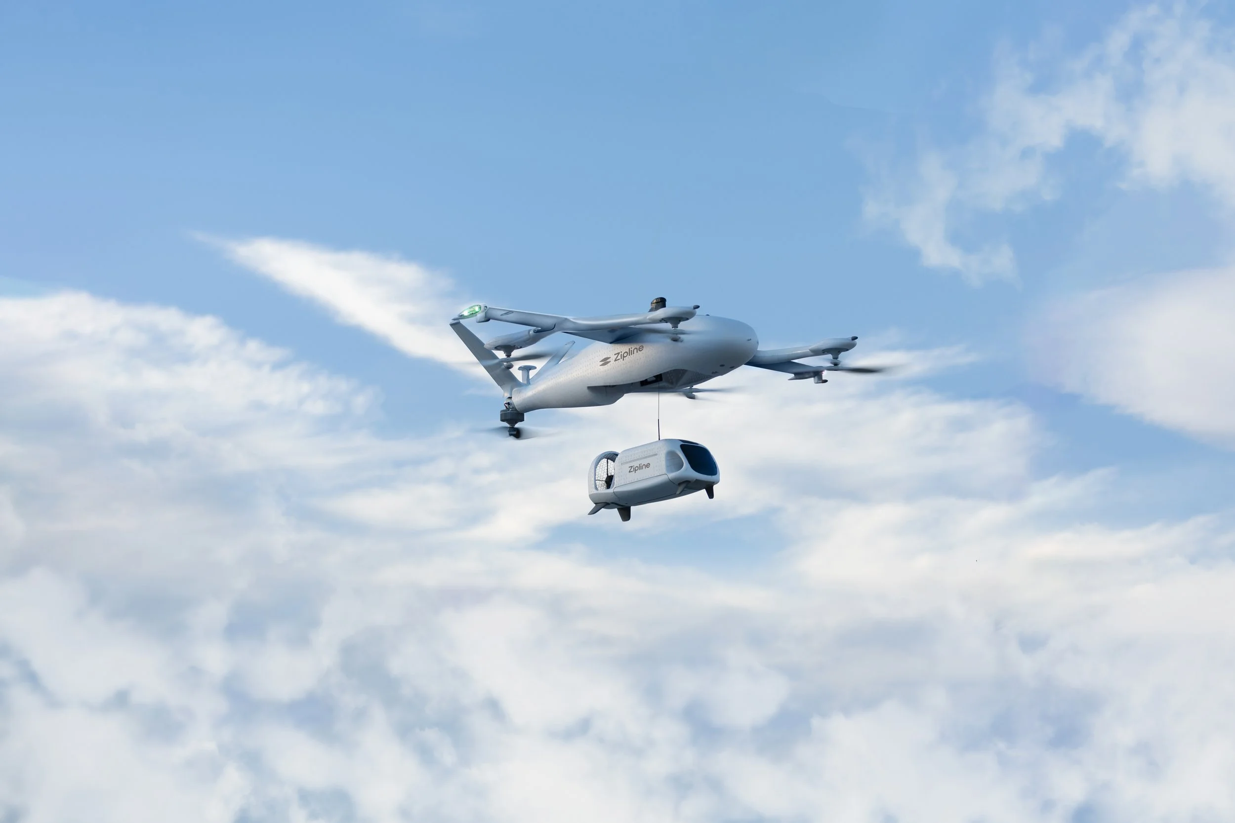 A plane-like commercial drone carrying a delivery pod against a partly cloudy sky.