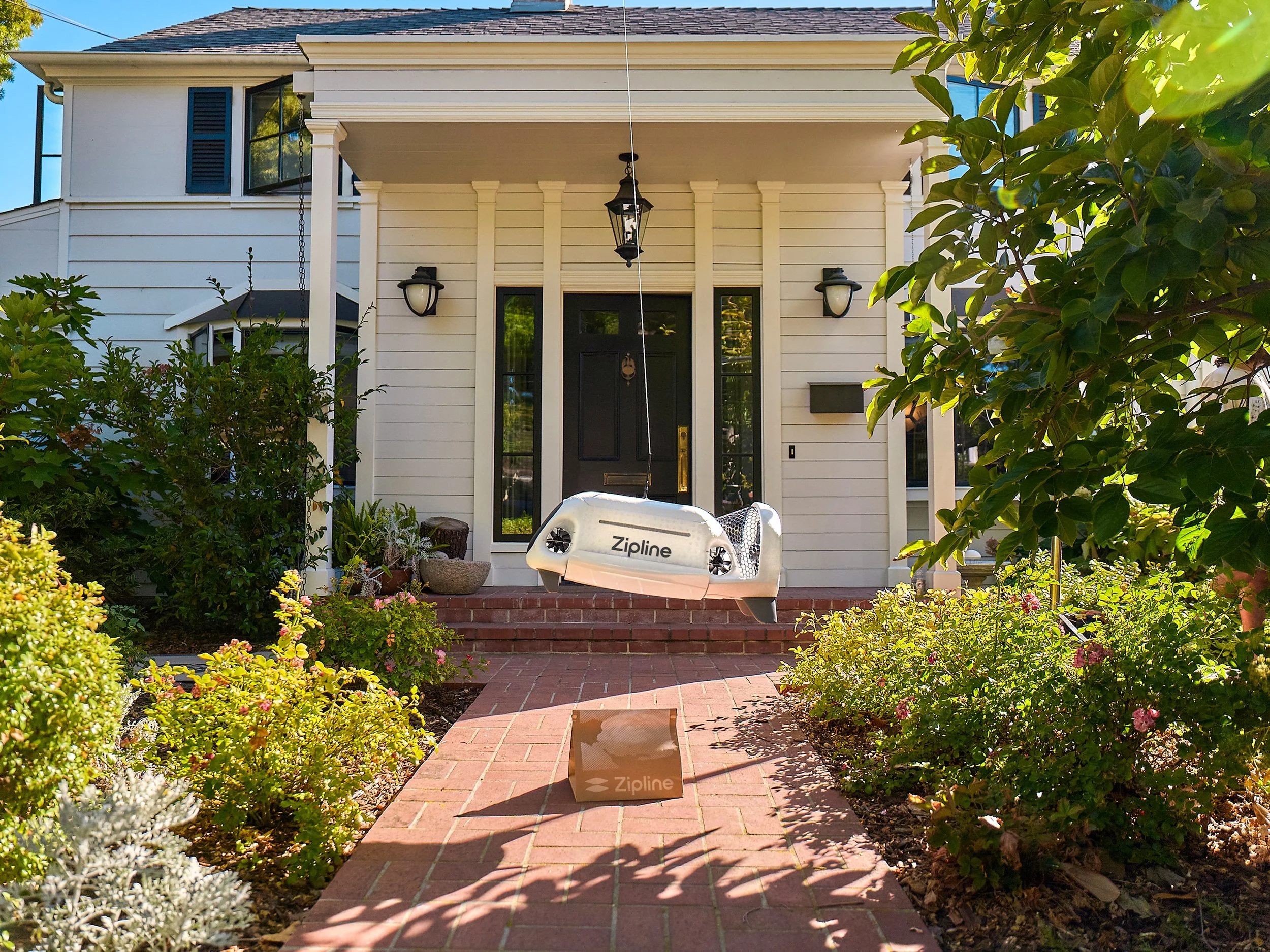 A delivery pod attached to a tether places a food delivery in a paper bag onto a front porch.