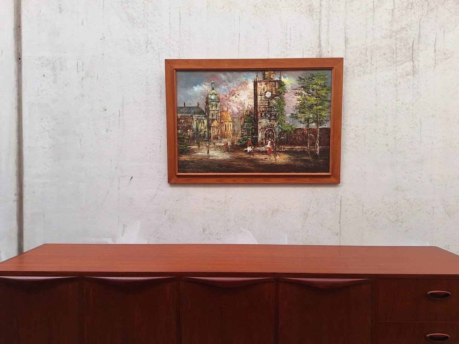 Vintage signed street scene oil painting styled above a teak sideboard.