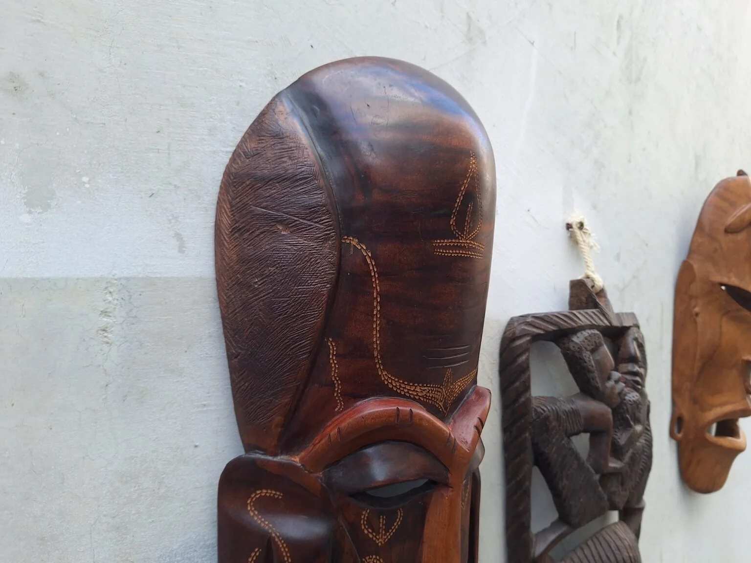 Close detail of the elongated timber mask showing the carved forehead pattern and surface finish.