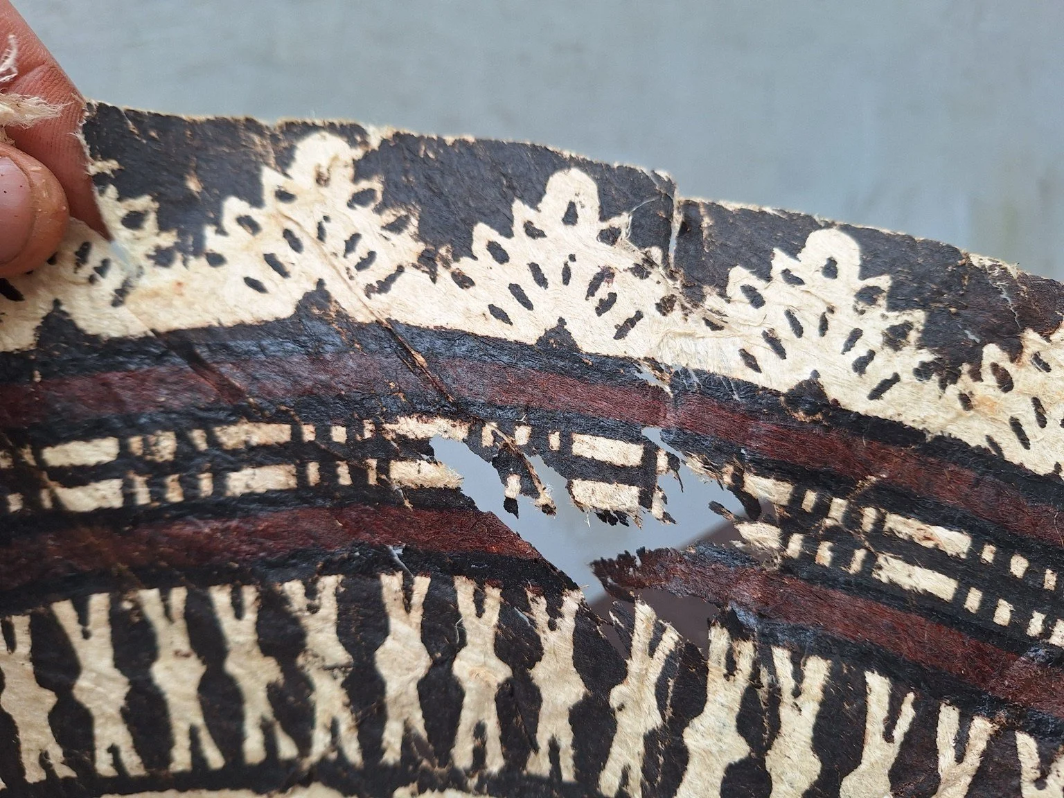 Detail of a substantial tear and missing barkcloth within the outer patterned bands.