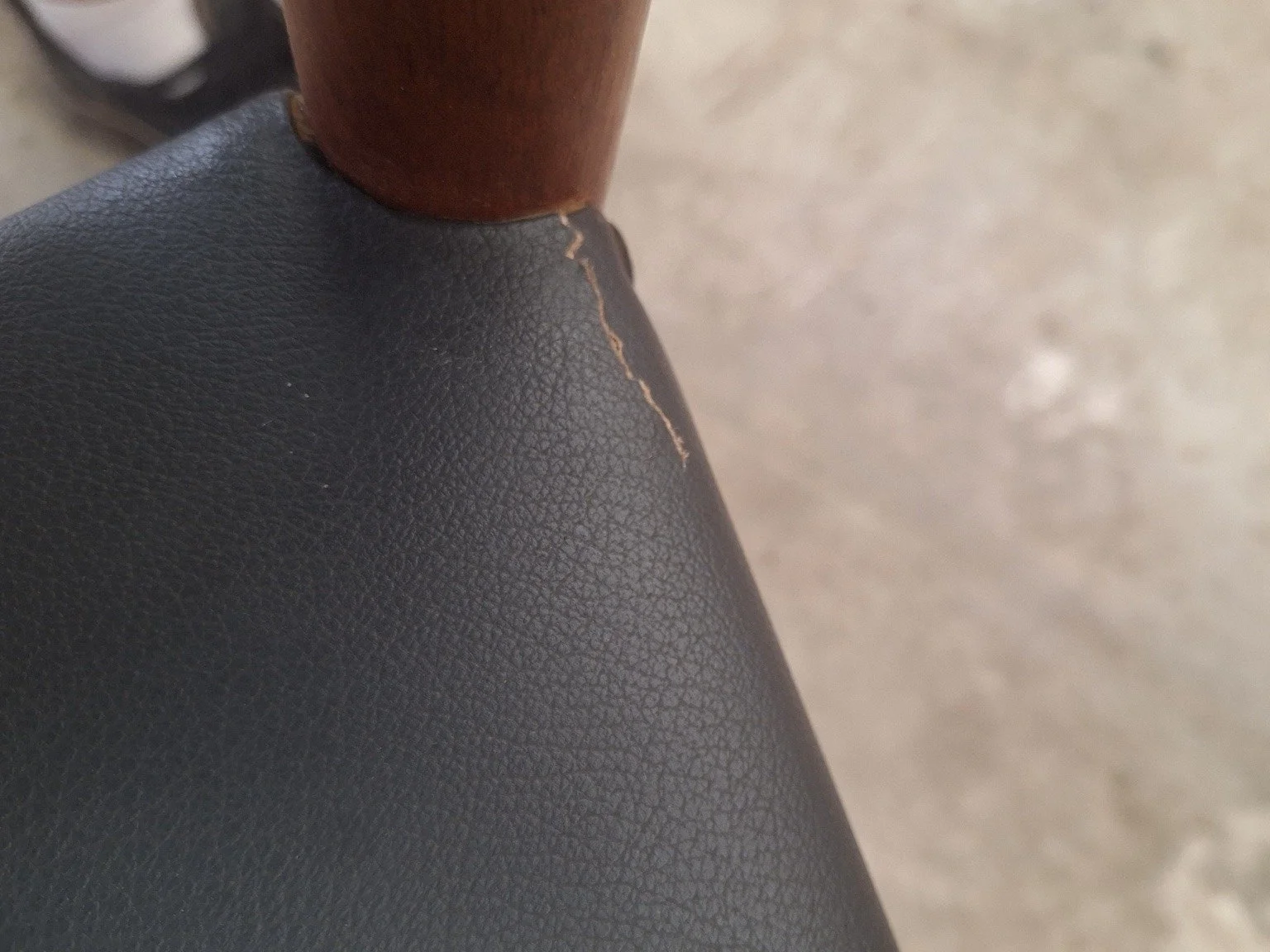 Close-up of upholstery edge wear beside a timber seat support.